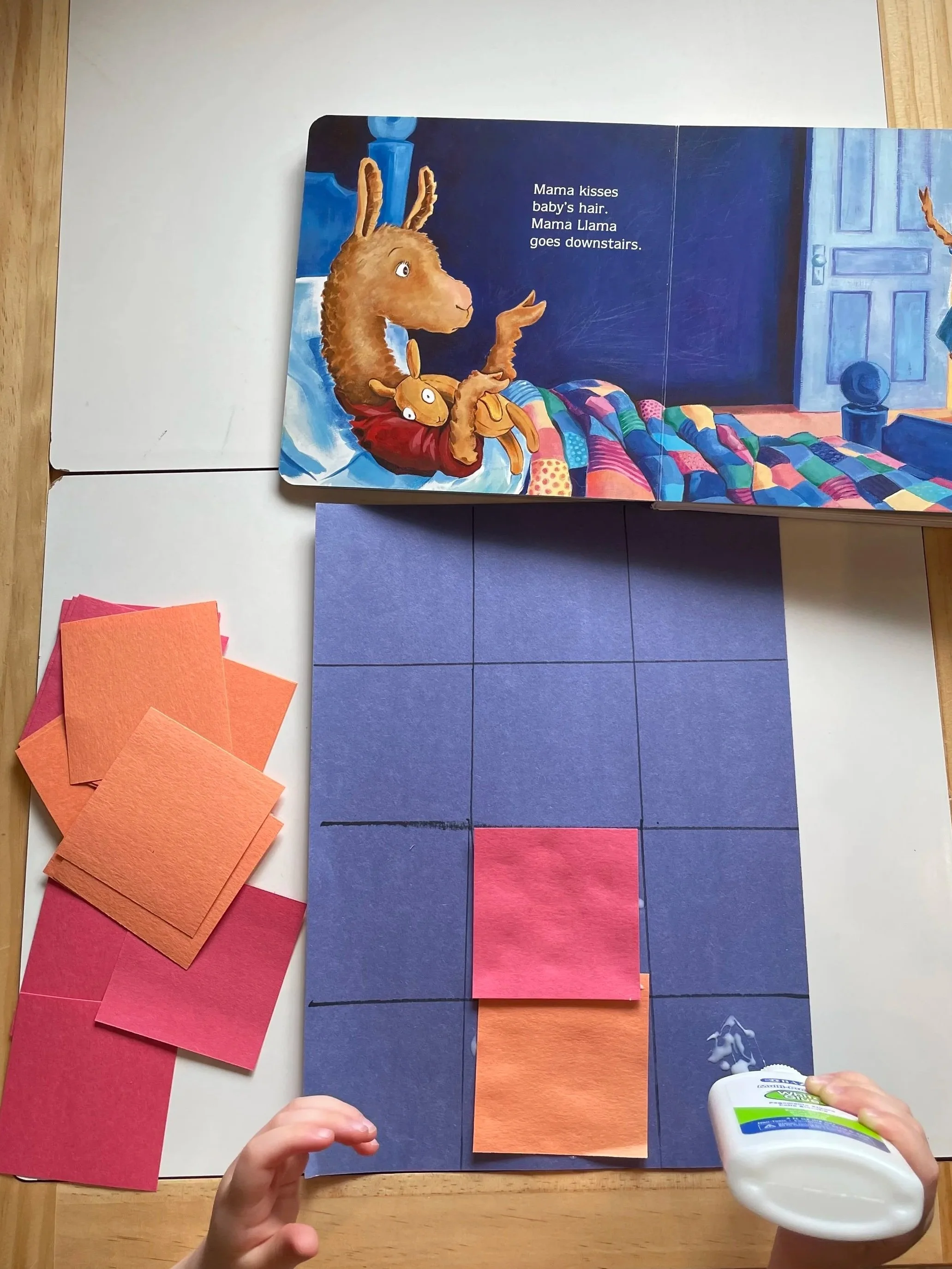 Children's book page with an illustration of a llama in bed and the text, 'Mama kisses baby's hair. Mama Llama goes downstairs.' The image shows blue, orange, and pink paper cutouts and a hand applying glue at the bottom right corner.