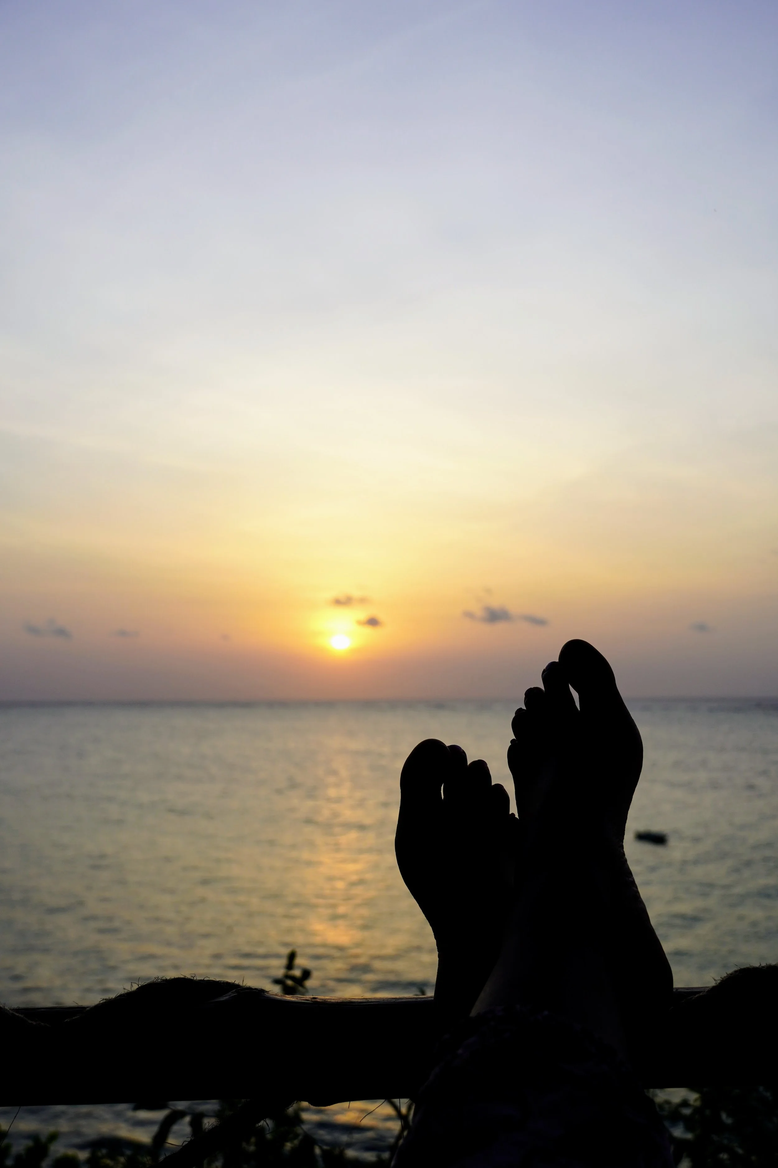 Silhouette of feet against a sunrise over the ocean with a clear sky.