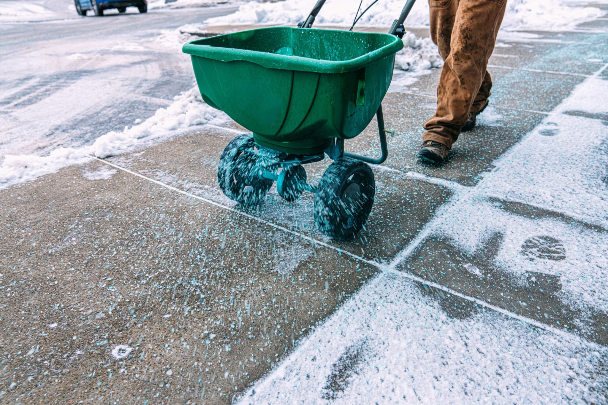 Person pushing a green snow shovel across a snowy sidewalk.
