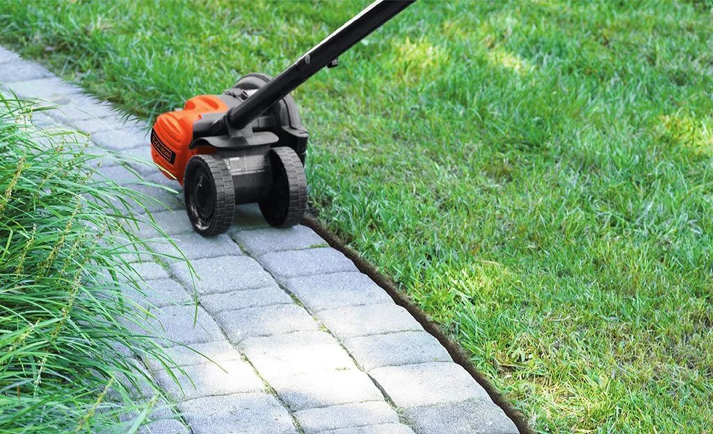 A garden lawn being maintained with a small electric or battery-powered weed trimmer along the edge of a brick pathway.