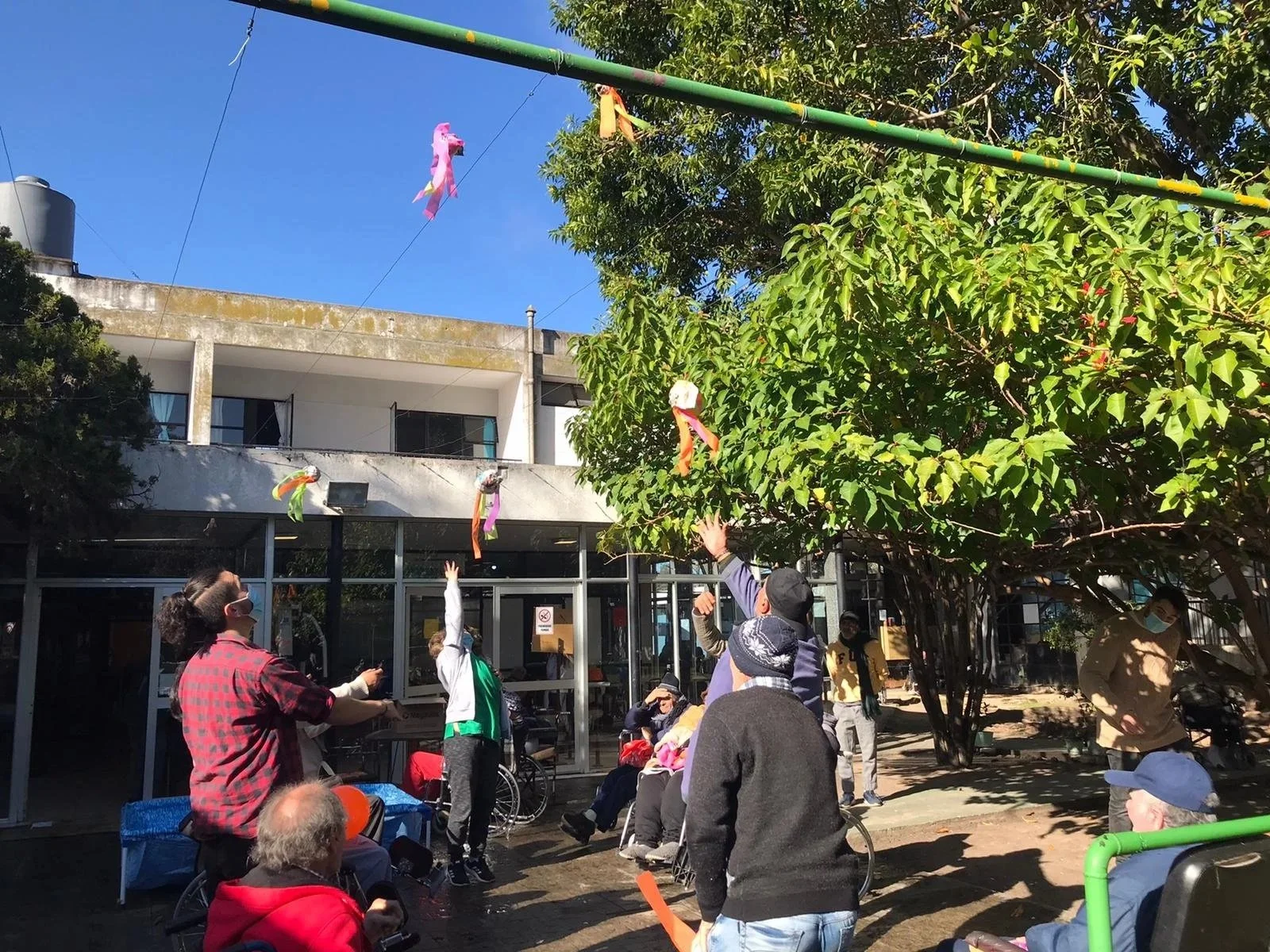 Personas celebrando en un espacio público con decoraciones de papel en el aire, algunos con sillas de ruedas y otros de pie, en un día soleado