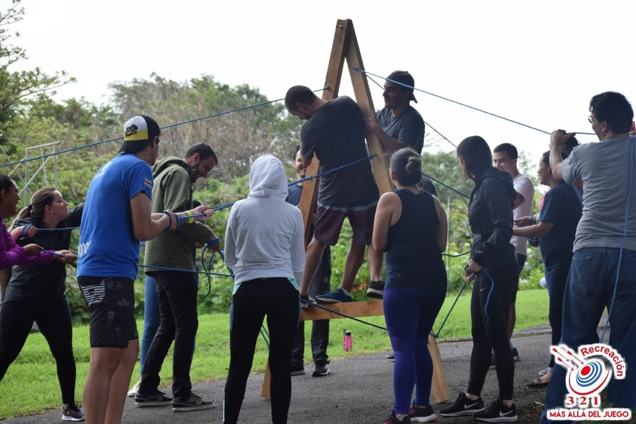 Grupo de personas participando en un juego de equilibrio con cuerda en un entorno natural.