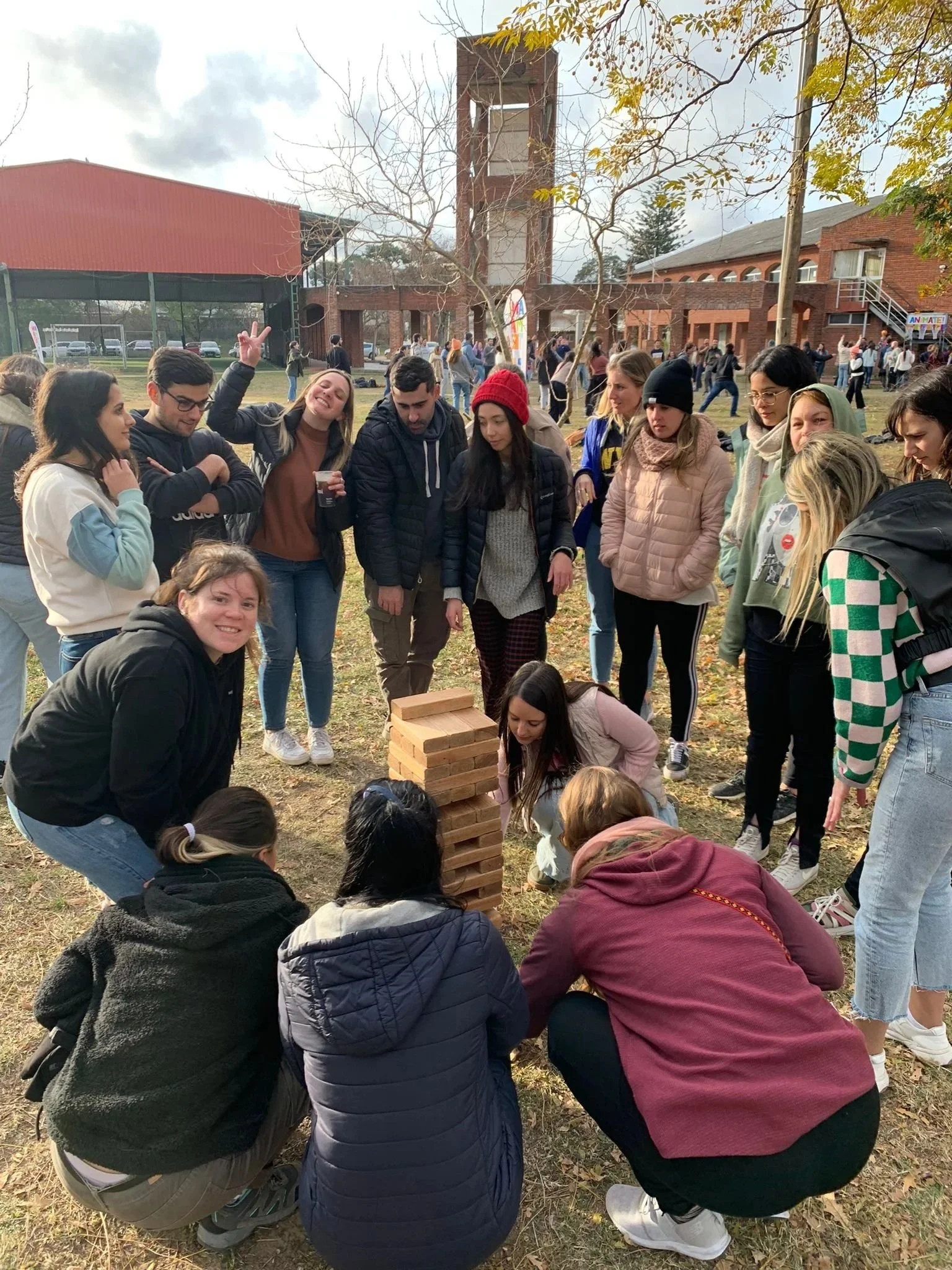 Grupo de personas jugando una torre gigante de bloques de madera en un parque durante el día.