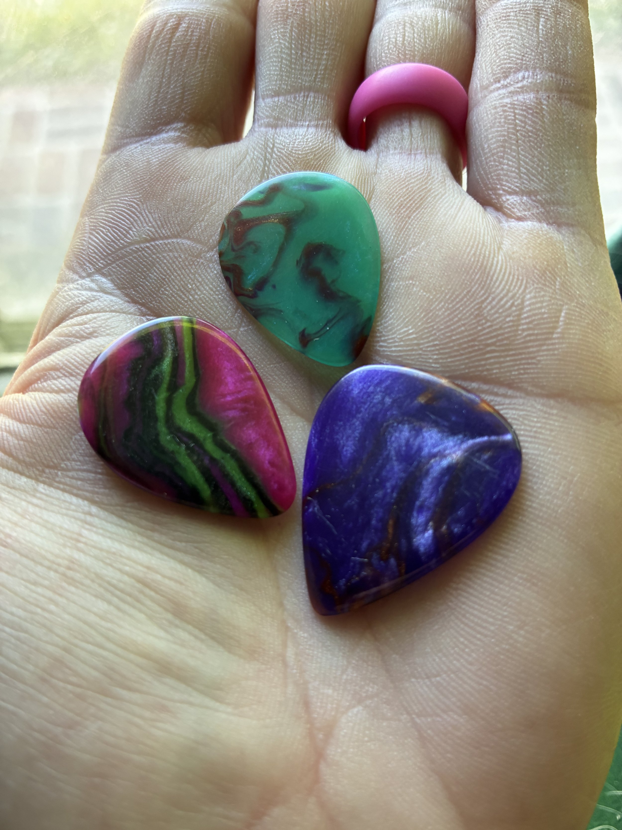 A close-up of a hand with four colorful guitar picks resting on the fingers.