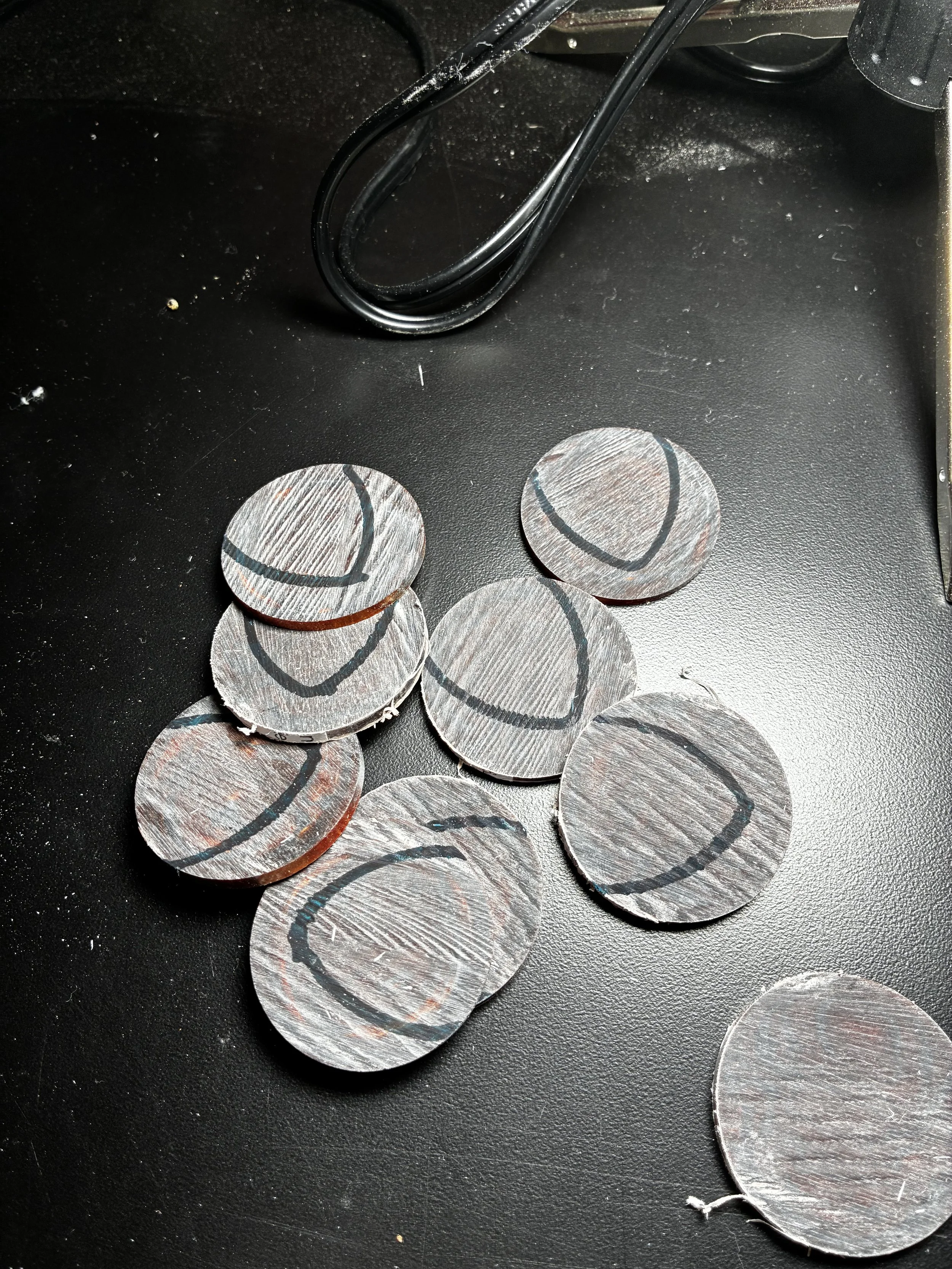 A black surface with several silver coins scattered on it. Some coins have black markings or lines, and a few black wires are also present near the top of the image.