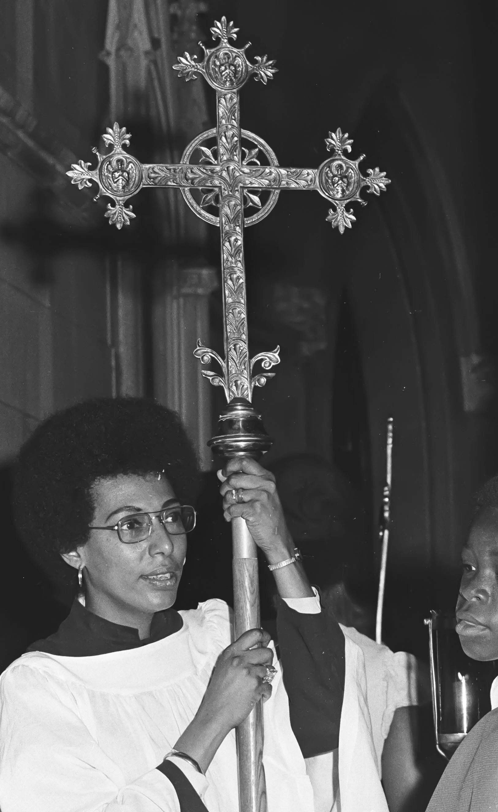 Barbara Harris holding a religious processional cross. Brad Hess black and white photograph, copyright Darlene O'Dell, Church of the Advocate, Philadelphia Eleven ordinations, July 1974, women priests, Episcopal, large crowd, press