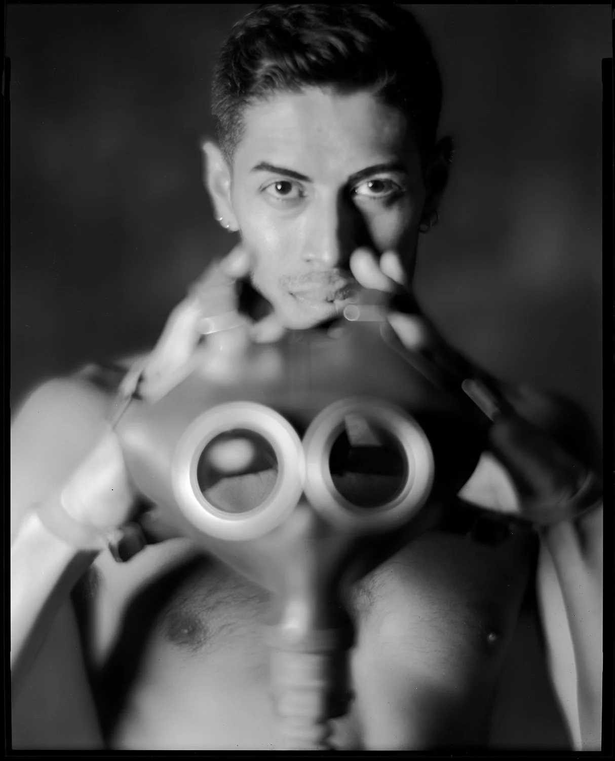 Black and white photo of a person taking a selfie with a camera, with the focus on the camera lens and the person's face visible in the background.