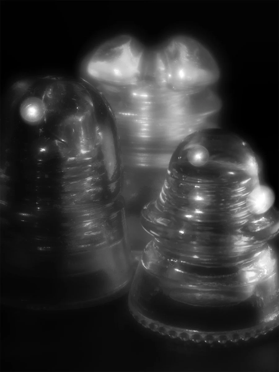 Close-up of three antique glass electrical insulators, with shiny surfaces and rounded bumps, set against a dark background.