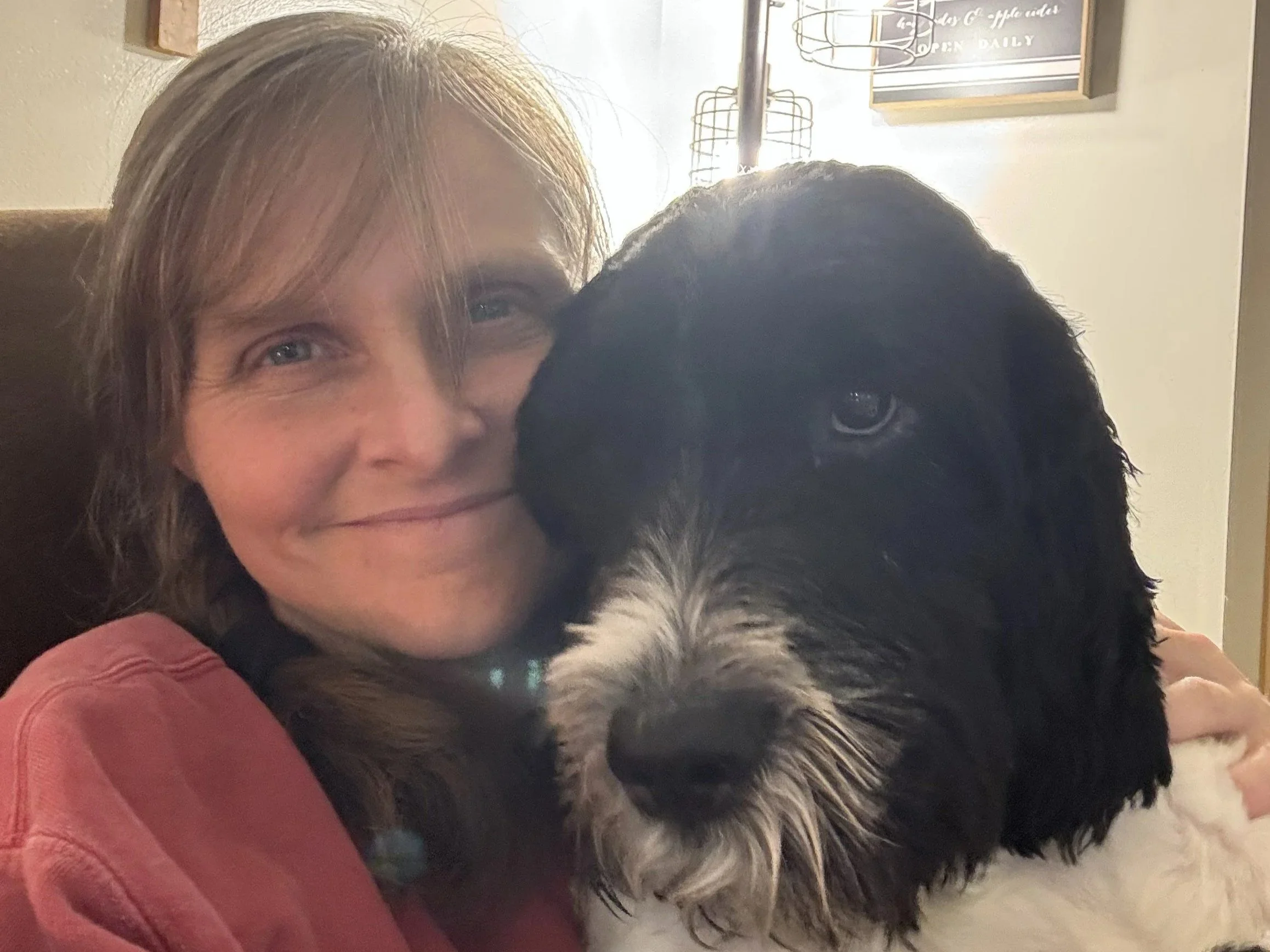 A woman smiling and hugging a black and white dog.