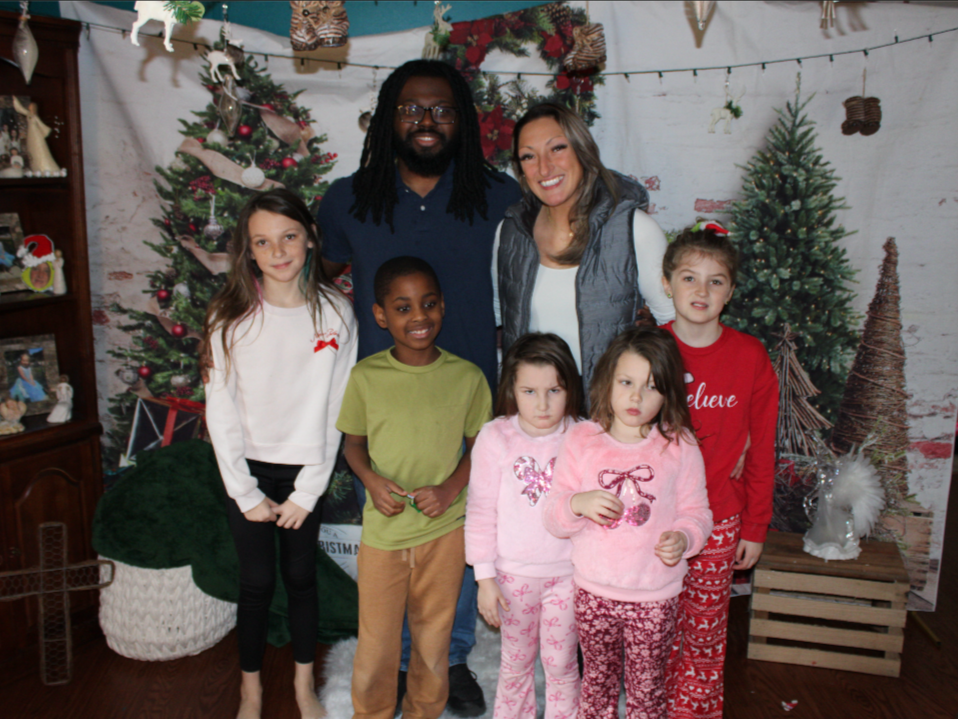 Group of children and adults posing in front of Christmas tree and holiday decorations.