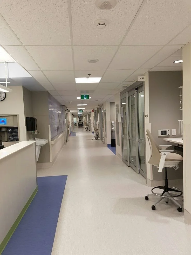 Hospital corridor with patient rooms, medical equipment, and a nurse station.
