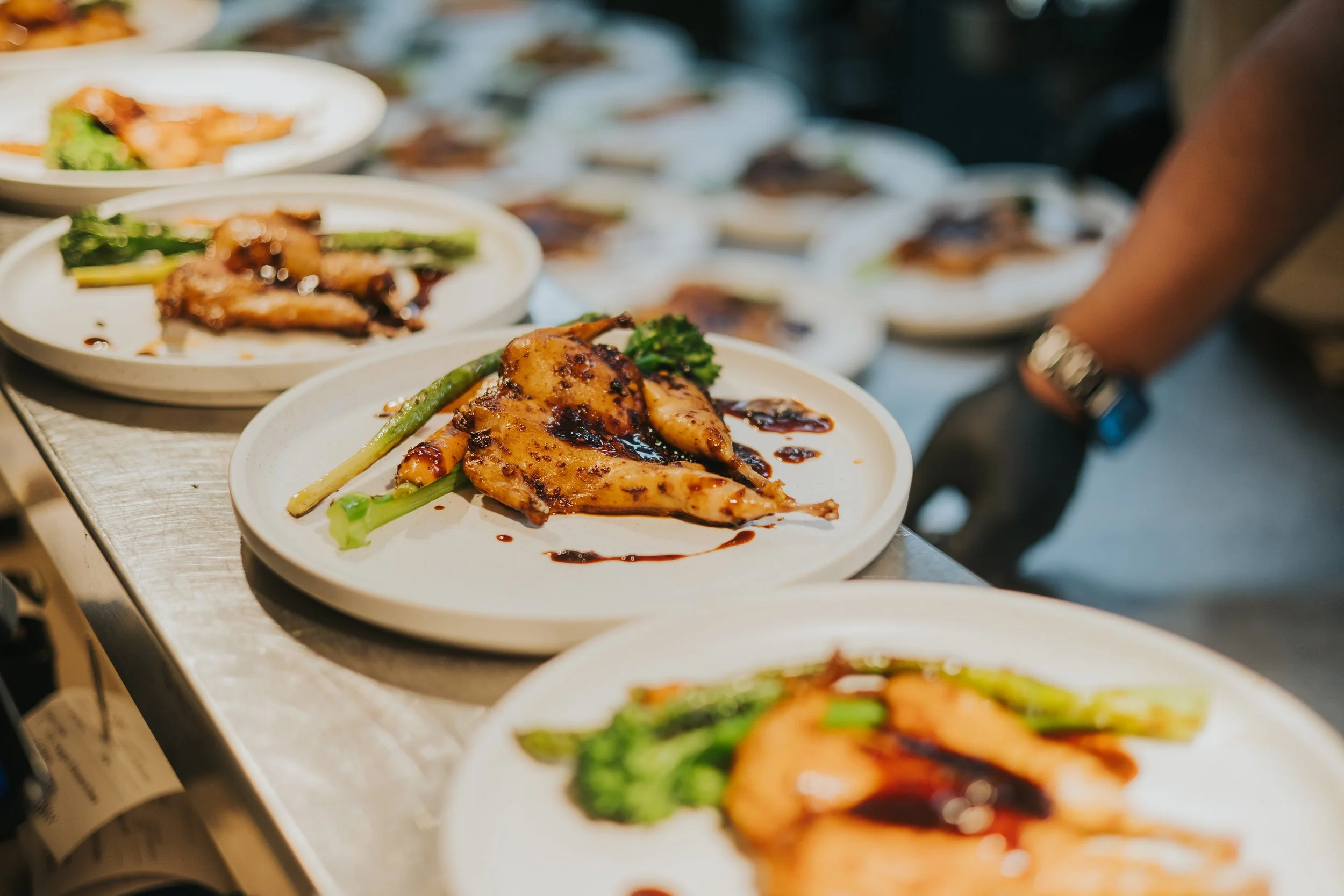 Plates of grilled chicken and vegetables with sauce on a countertop at a buffet or food service setting.