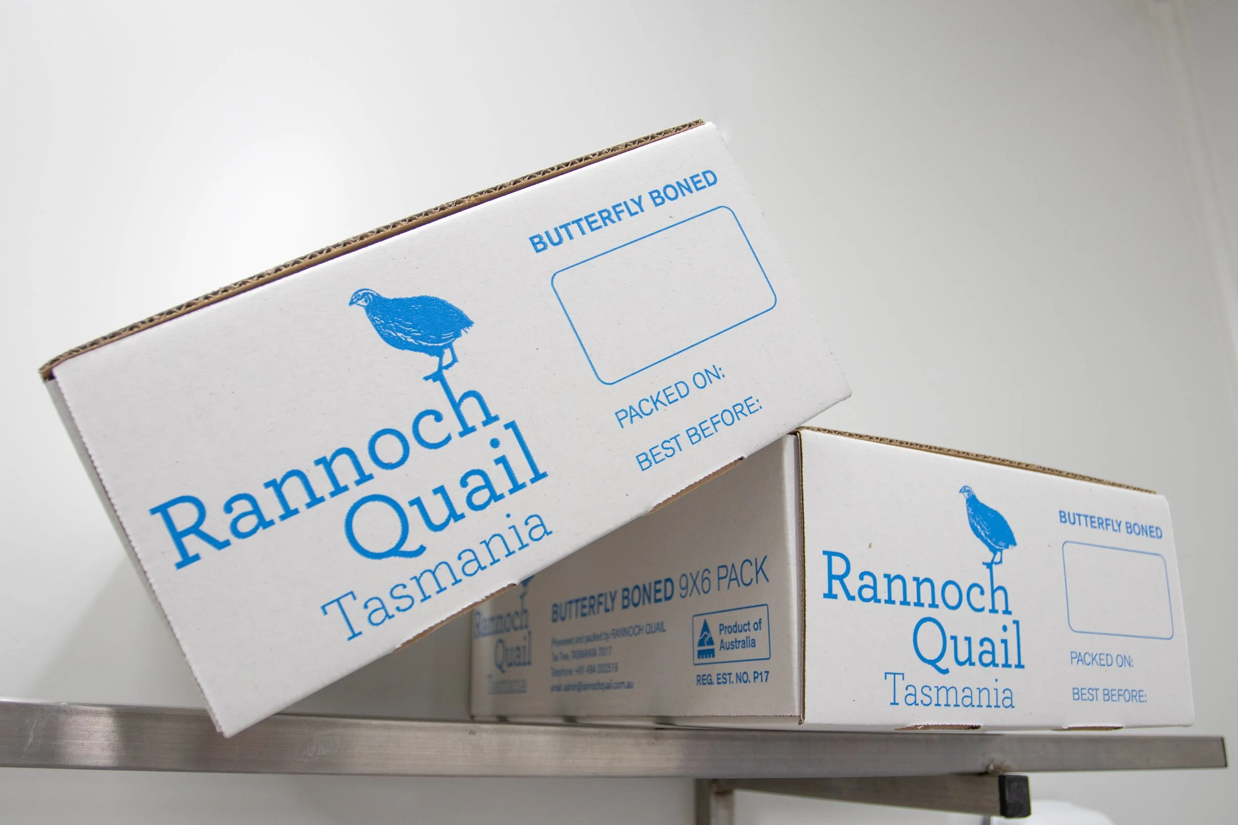 Close-up of a box labeled 'Rannoch Quail Tasmania' with a blue illustration of a quail, placed on a metallic surface.