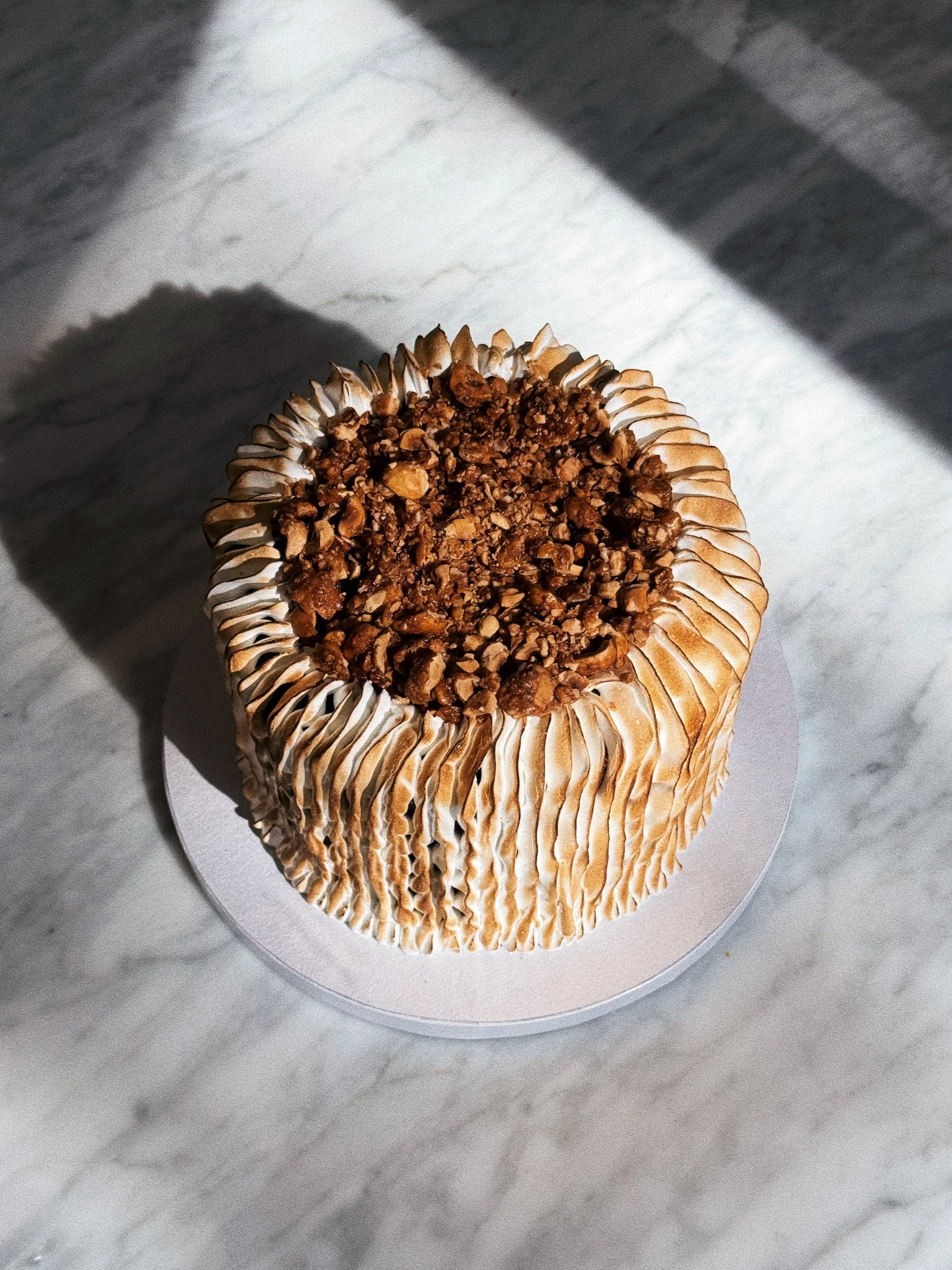 A cupcake with a swirl of frosting topped with chopped nuts, placed on a white doily on a gray marble surface.