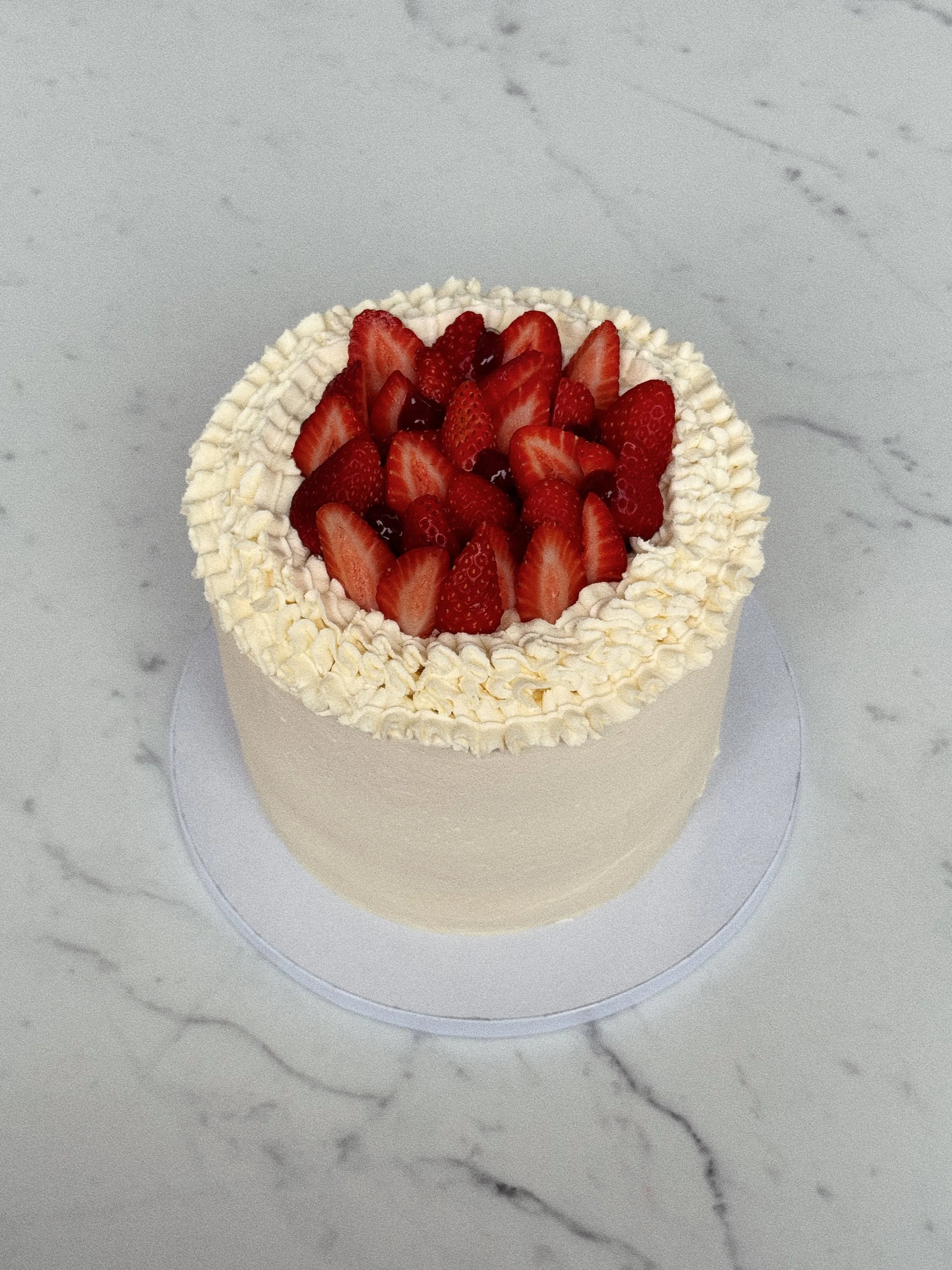 A cake decorated with fresh strawberries and cream on top, surrounded by piped cream, on a marble surface.