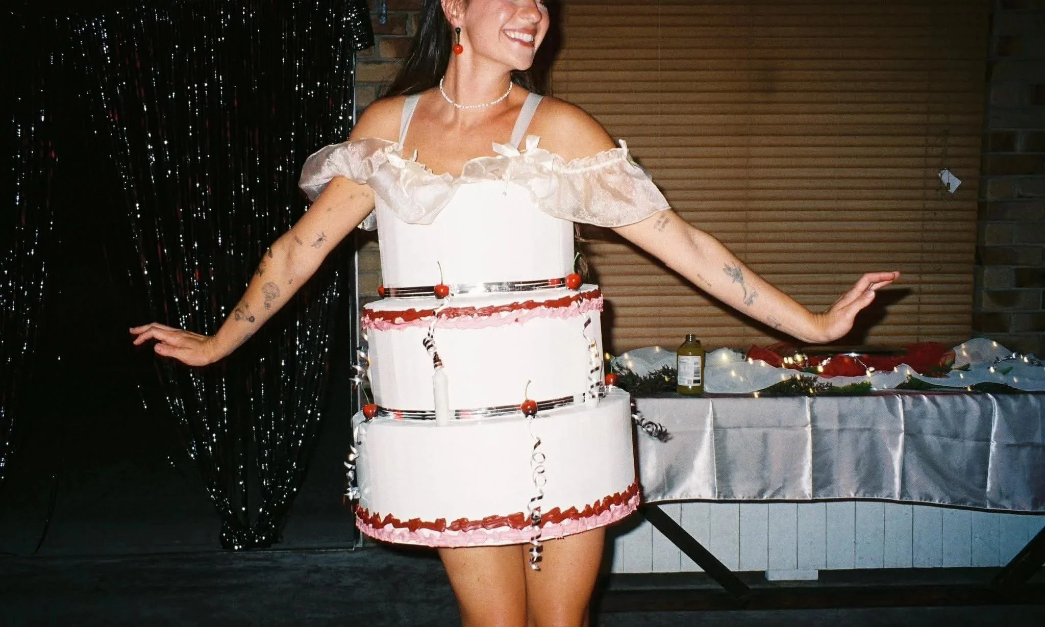 A woman in a dress with a cake-shaped skirt, smiling and wearing red earrings, a pearl necklace, and Christmas-themed decorations on a table.