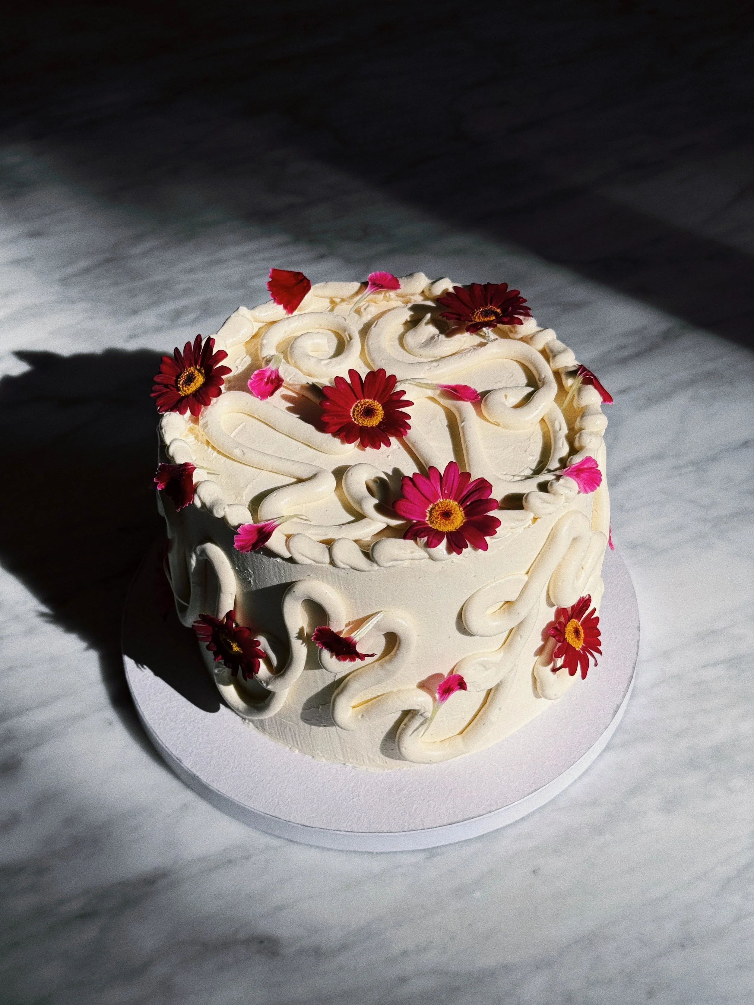 Round white cake decorated with red and pink flowers and white icing.
