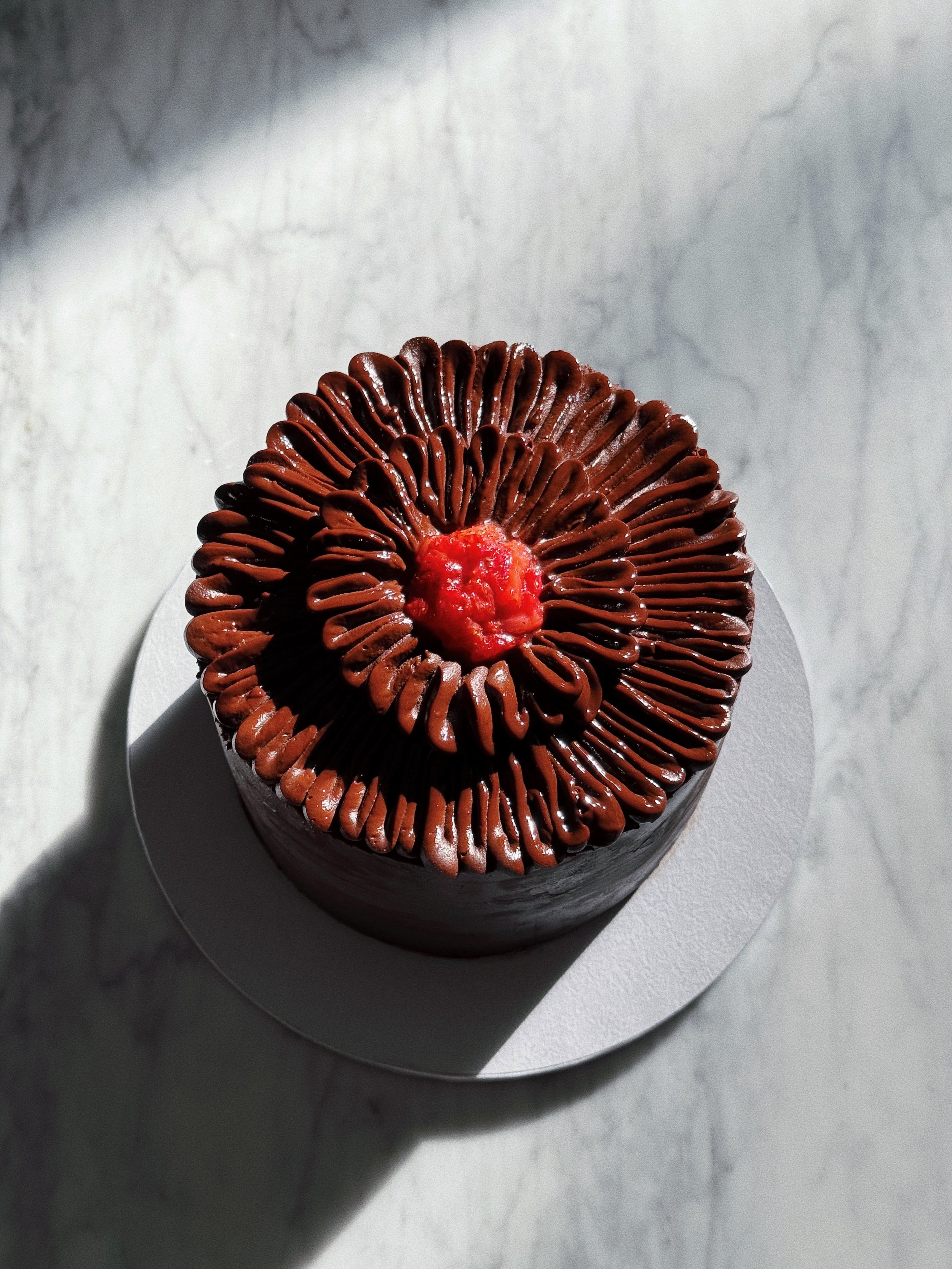 A chocolate cupcake with swirled chocolate frosting and a small red decoration on top, placed on a silver platter.