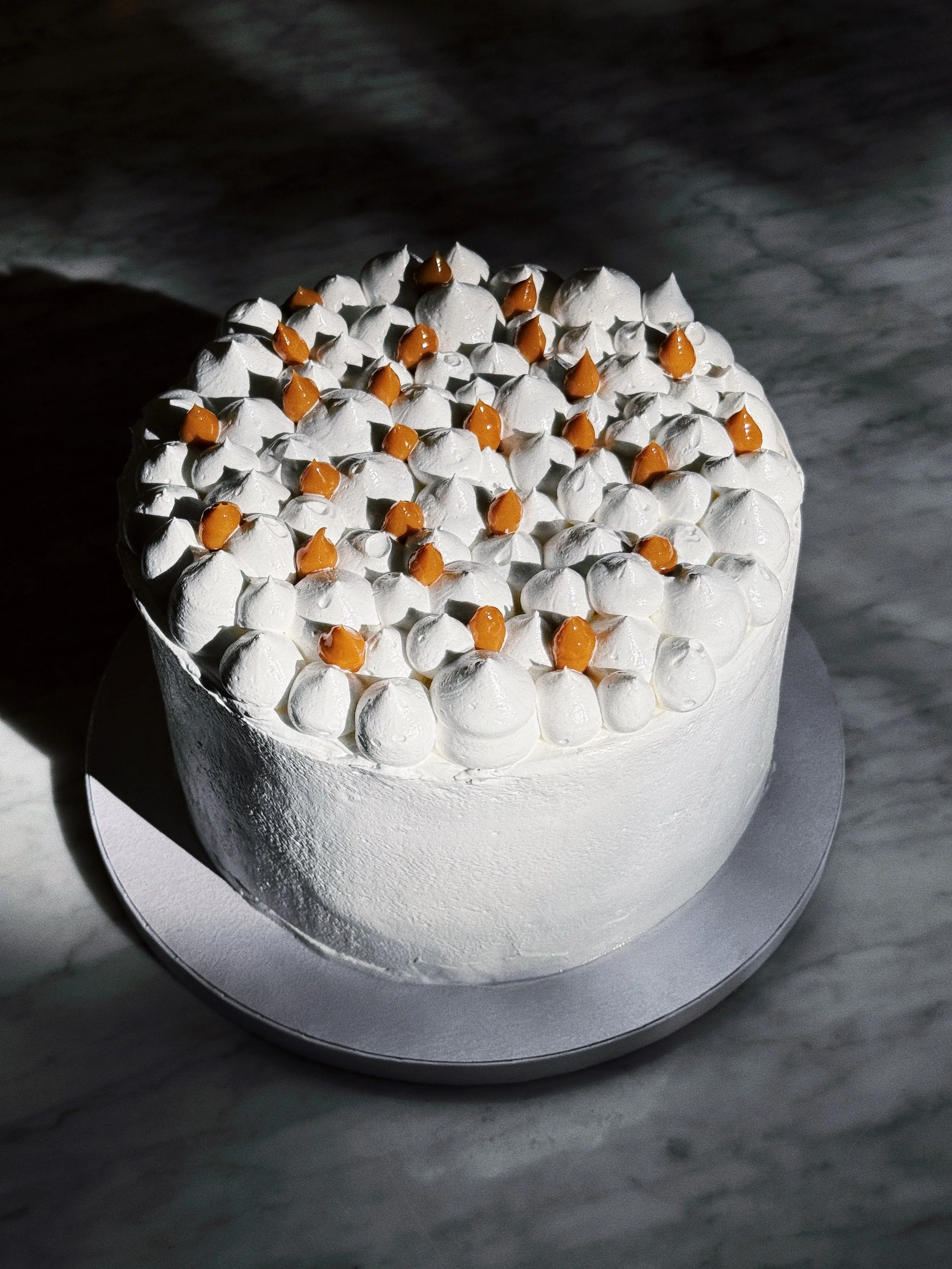 Cake with white italian meringue and dulce de leche decorations on top, displayed on a whitecake board.