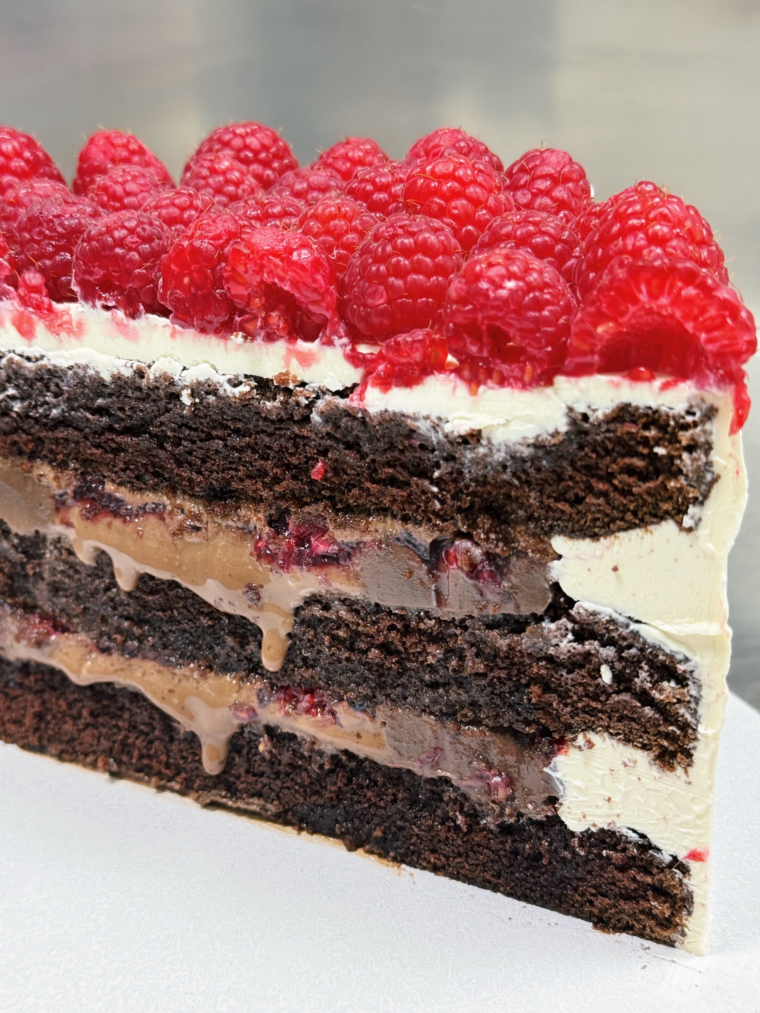 Slice of chocolate cake with layers of chocolate ganache, raspberries, berries jam, topped with fresh raspberries and finished with Swiss buttercream.