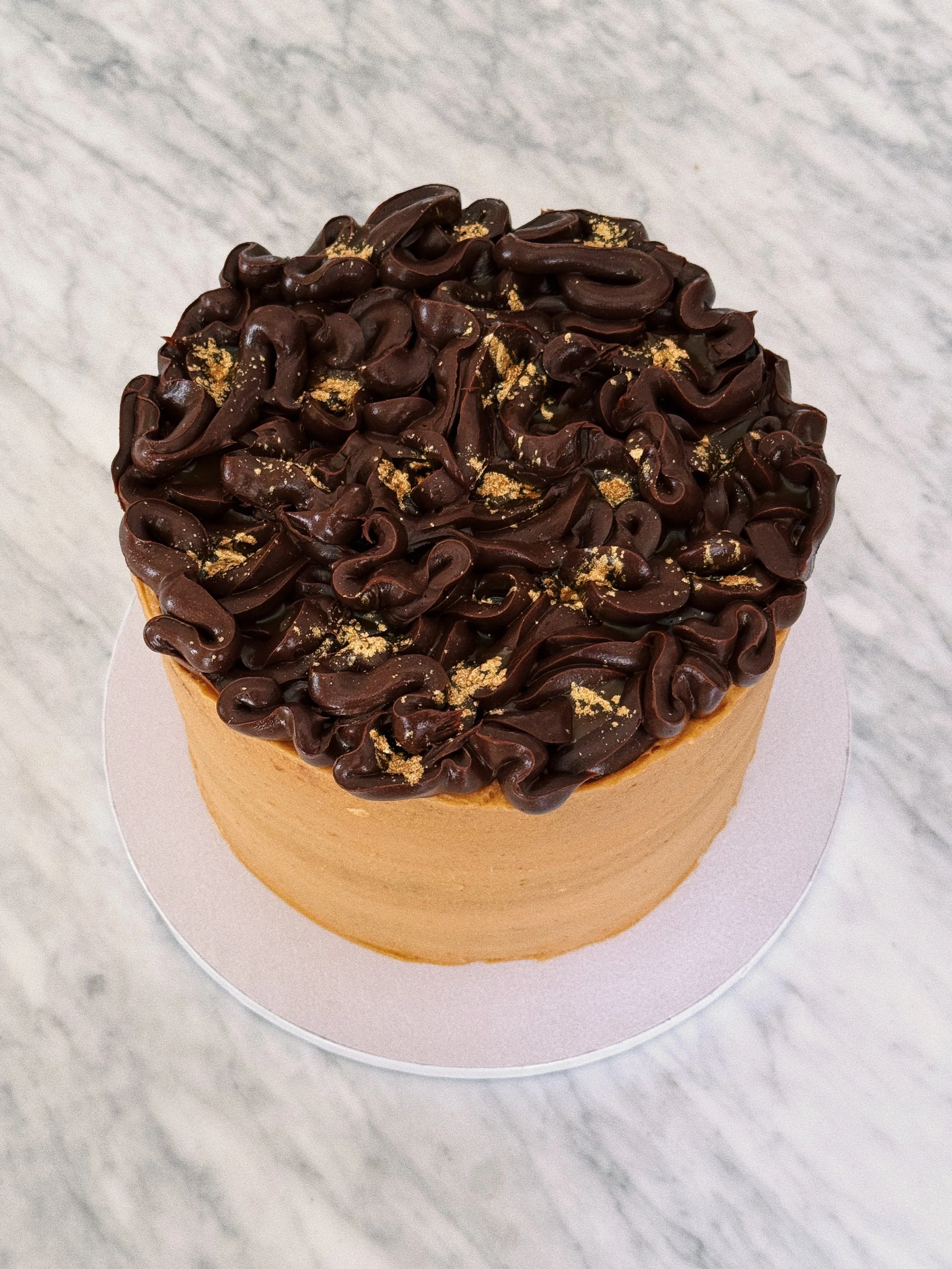 A chocolate and salted caramel cake topped with chocolate crèmeux, with a sprinkle of gold dust.