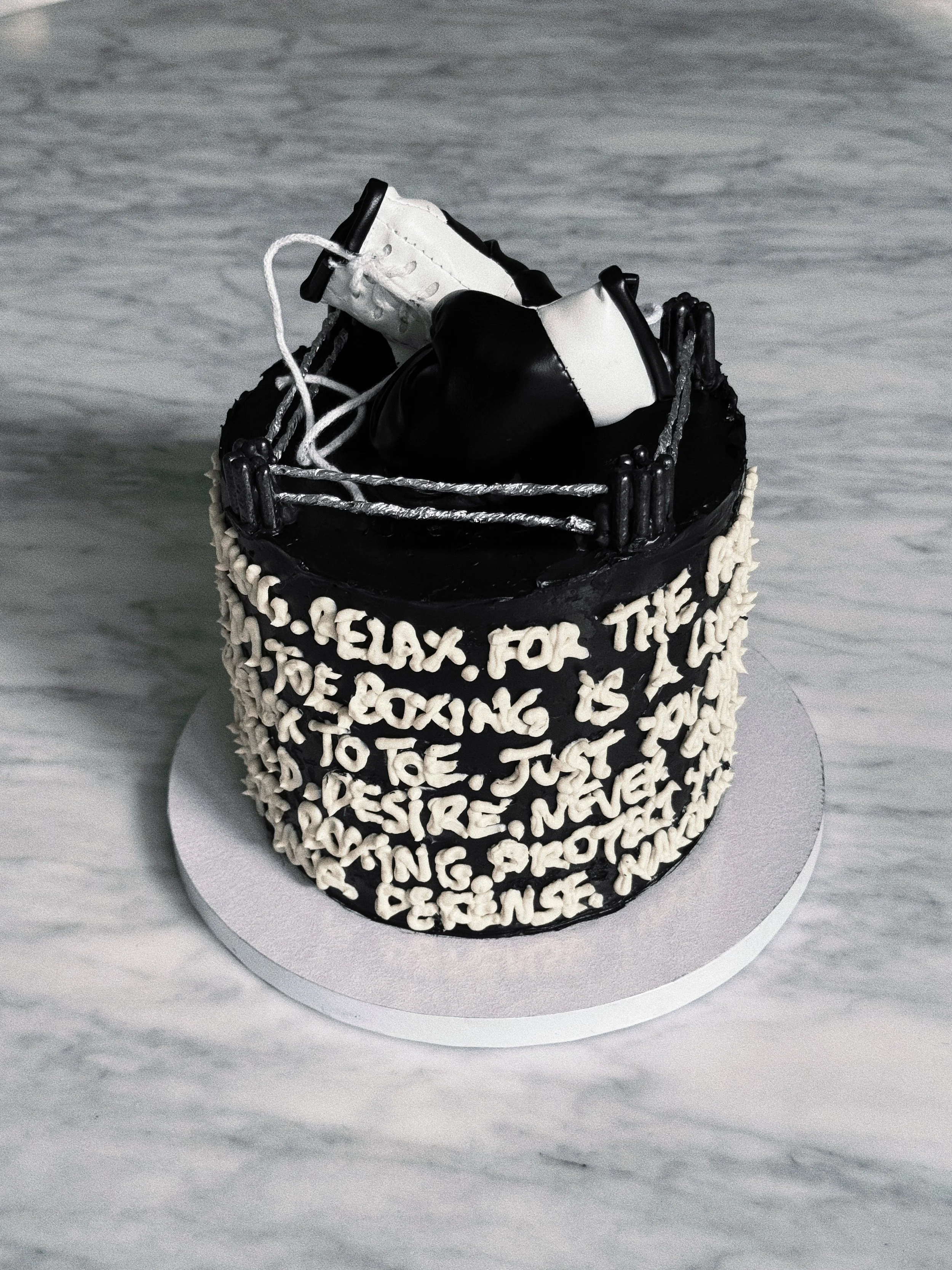 A cake with black and white icing, decorated with white letters around the sides, and a hockey skate on top.