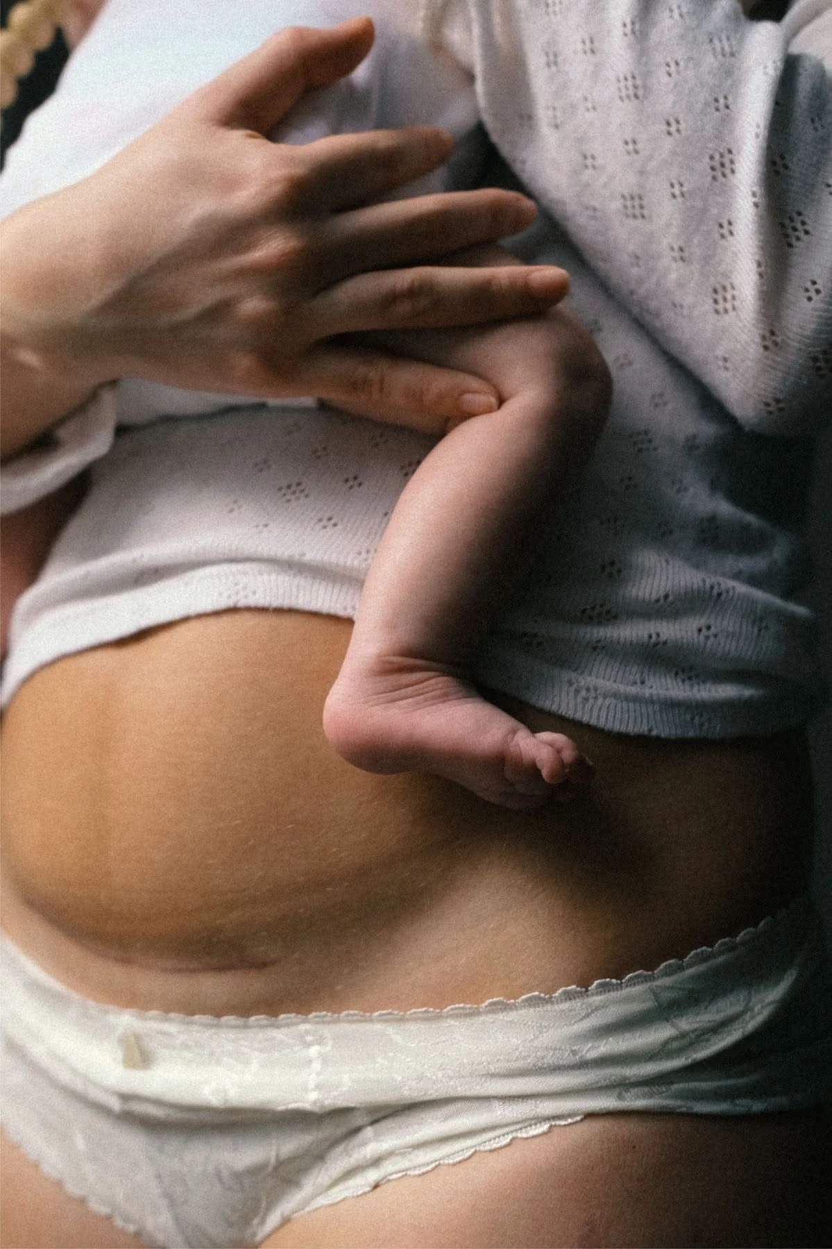 Close-up of a birth scene with a newborn baby lying on a person's chest, and a hand gently touching the baby's head, with the person wearing a hospital gown.