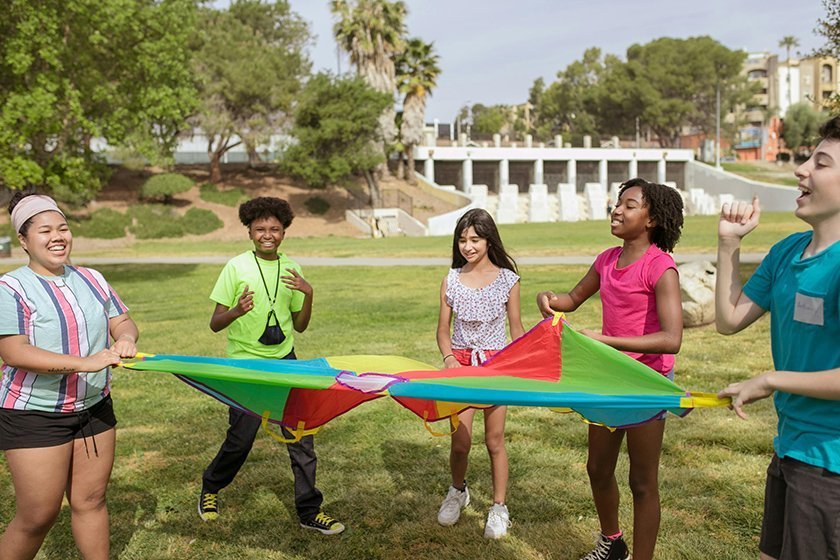Group of children playing with a colorful parachute outdoors in a park.