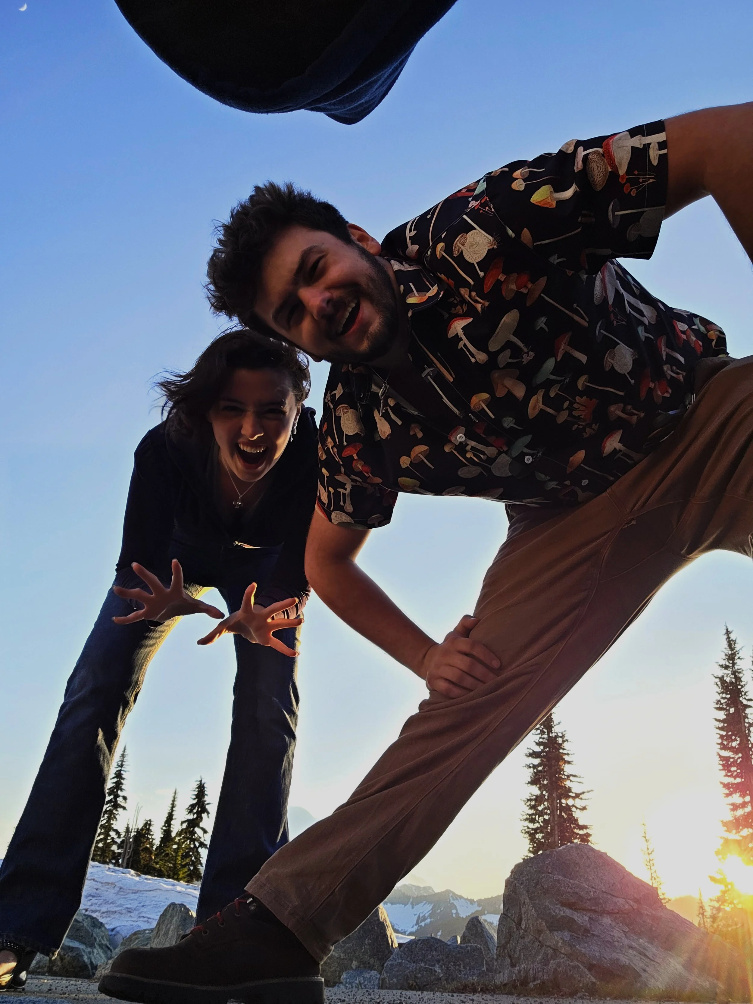 A group of people outdoors during sunset, with rocks, trees, and mountains in the background, smiling and enjoying each other's company.