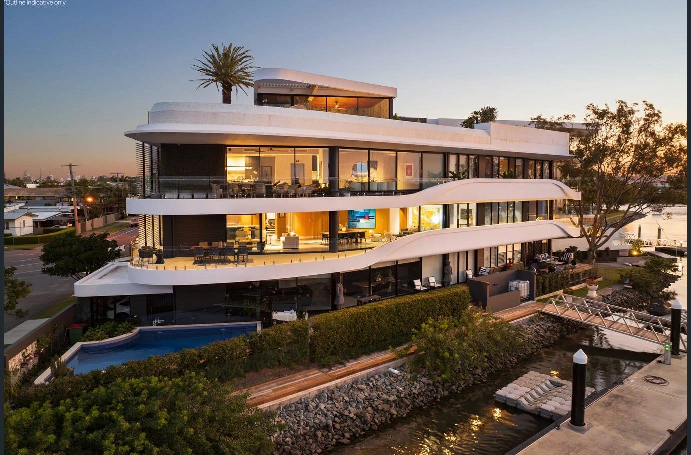 Modern multi-story building with curved balconies, large glass windows, outdoor seating areas, a small pool, and a dock by a waterway during sunset.
