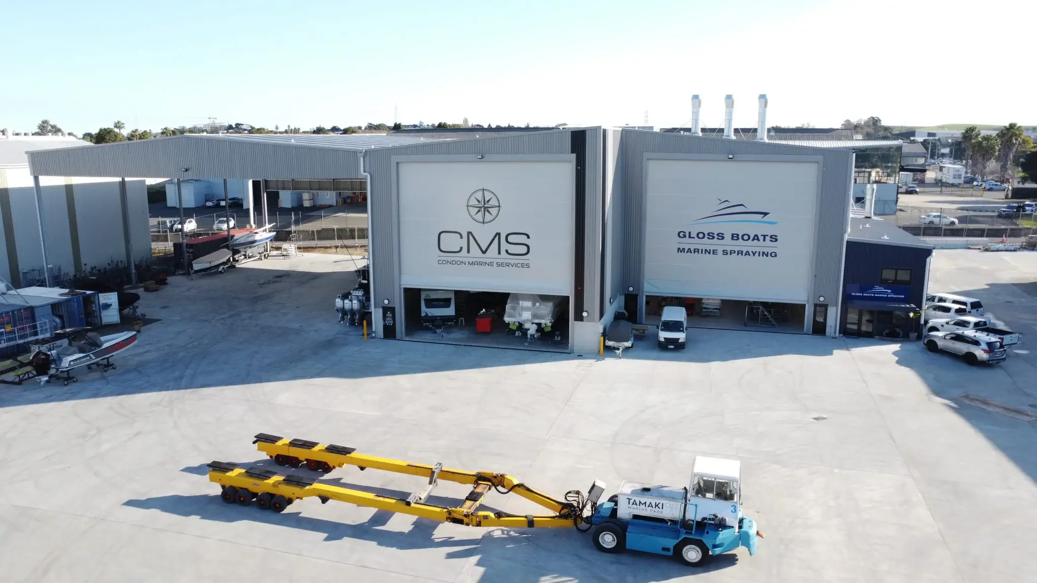 Industrial boat dealership with boats, trailers, and vehicles outside, featuring the logos CMS and Gloss Boats Marine Spraying.