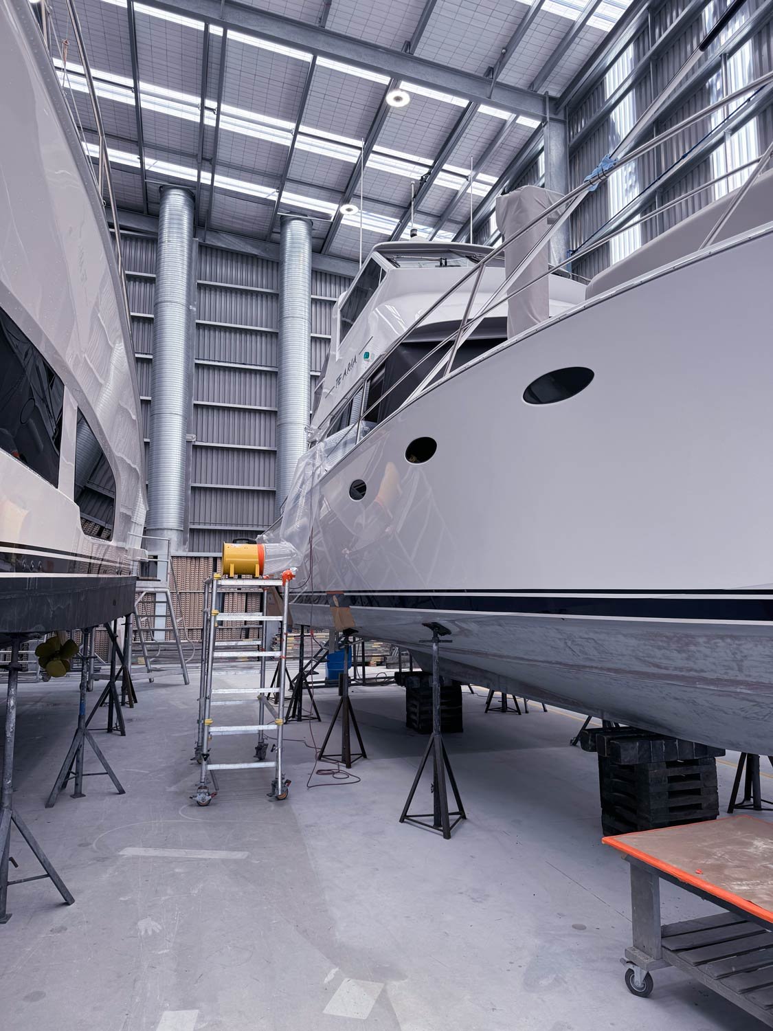 Large white yacht inside a boat storage or maintenance facility, supported on temporary stands with equipment nearby.