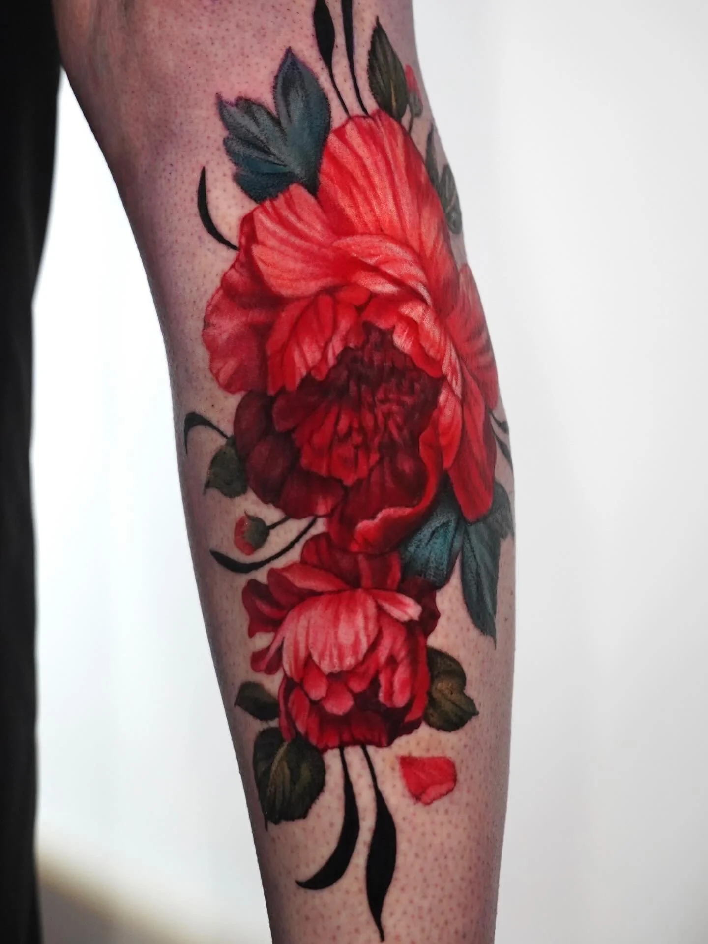 Close-up of a tattoo of red flowers and green leaves on a person's arm.