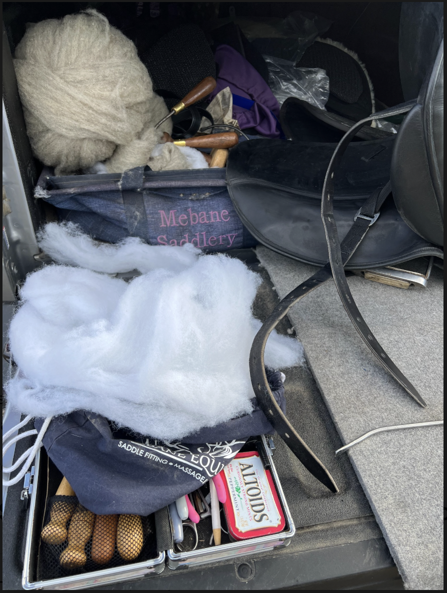 Professional saddle fitting tools and natural wool flocking material used by independent consultant Tara Mebane for custom saddle flocking adjustments.and saddling supplies, including brushes, a saddle, and grooming tools, inside a vehicle trunk.