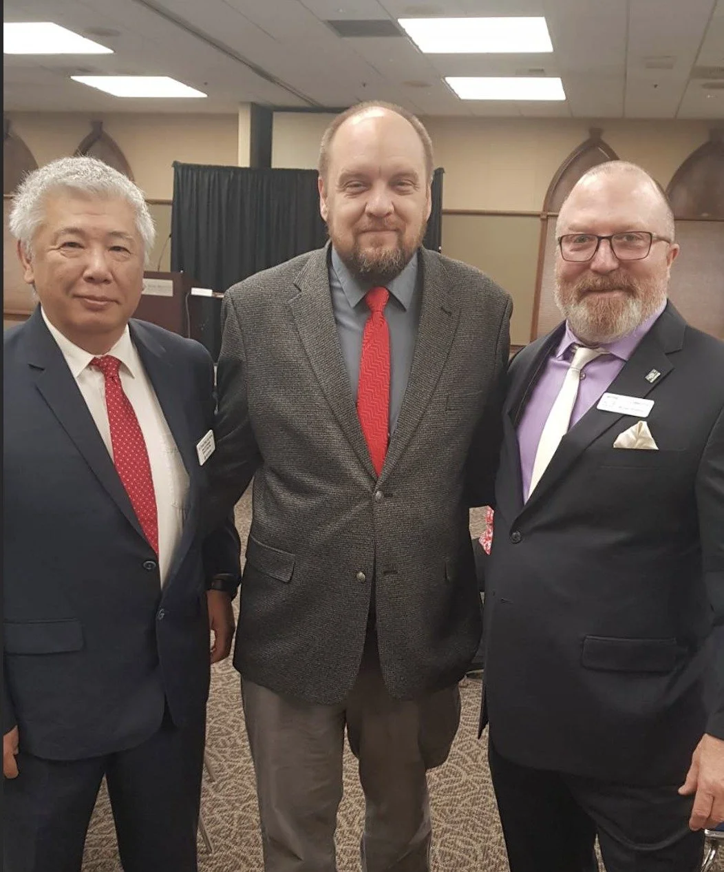 Three men in business suits posing together at a formal event.