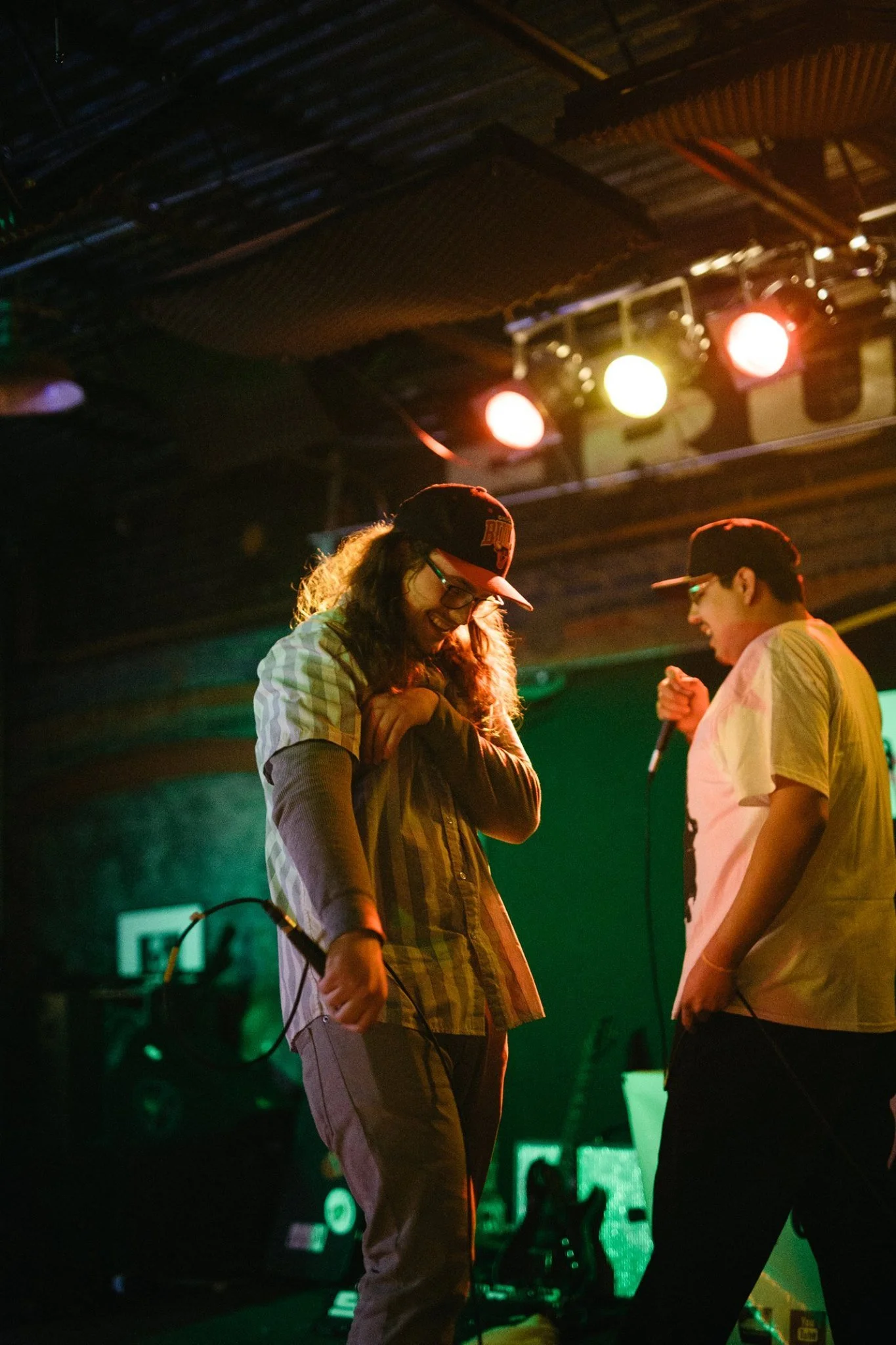 C. Boy and Symon Palmer on a stage performing with microphones, illuminated by stage lights, with one smiling and the other focused.