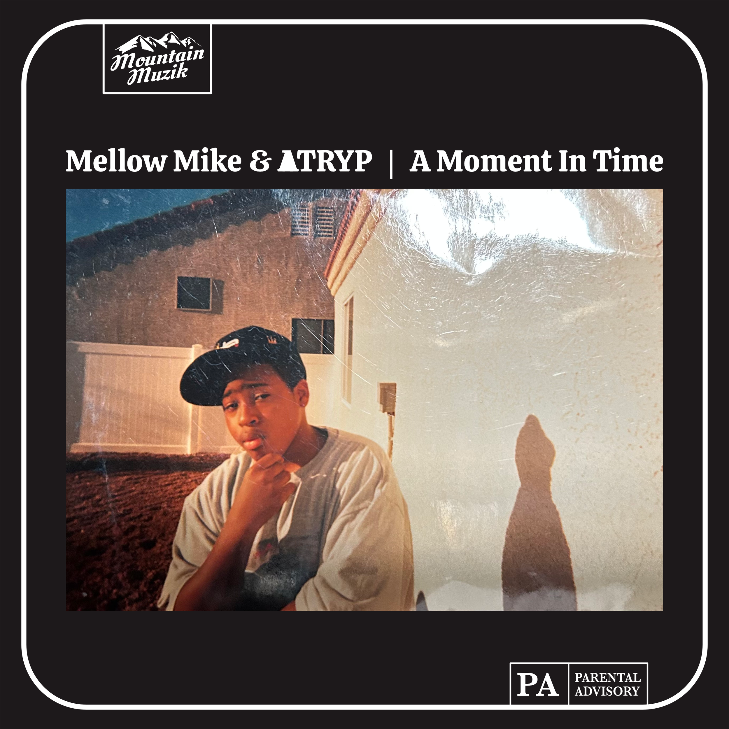 Album cover of a young Atryp wearing a baseball cap and posing for the camera in his yard. With a black border, saying Mellow Mike & Atryp - A Moment In Time.  Arranged with a parental advisory sticker and Mountain Muzik logo.