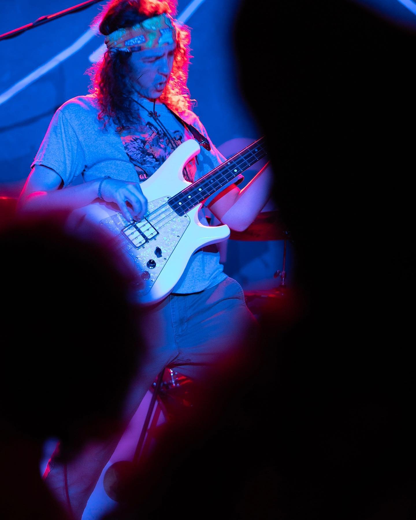 Carl from STiLGONE playing an electric bass guitar on stage, illuminated by red and blue stage lights