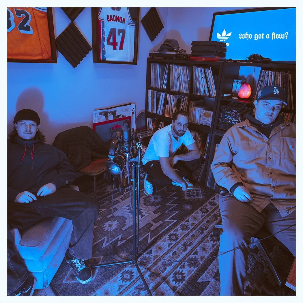 Cover art for single "Who Got a Flow?" There are three men in a recording studio with musical equipment, bookshelves, and sports jerseys on the wall. A large monitor displays the text 'who got a flow?'