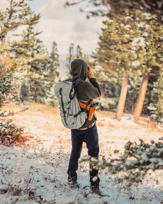 Twelve Clouds with a backpack hiking in a snowy forest with trees.
