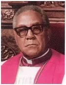 Portrait of a man wearing dark sunglasses, a pink jacket, and formal clothing.