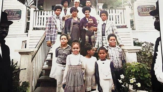 A large group of children and adults gathered on stairs outside a house for a group photo.