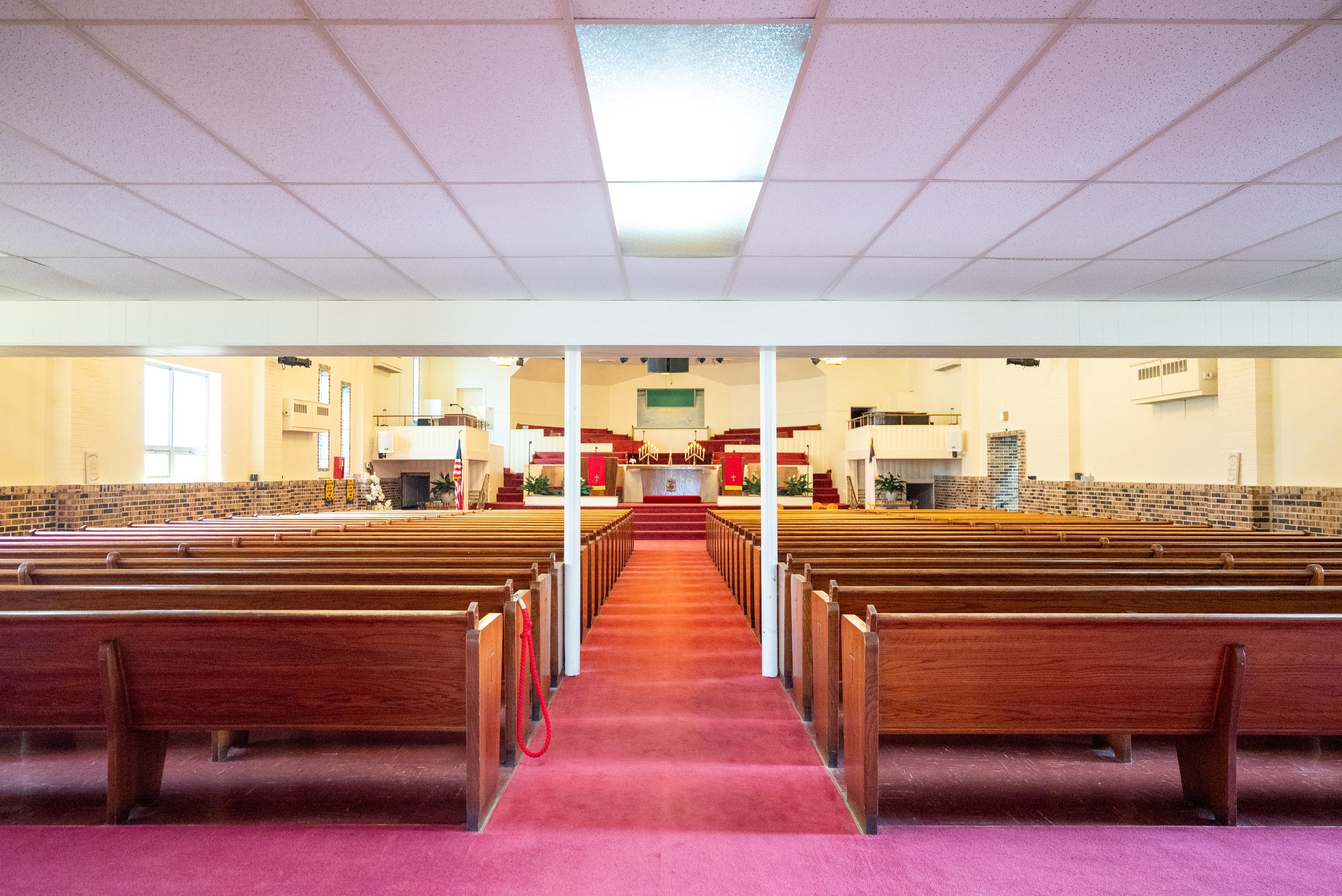 Interior of a church with wooden pews, red carpeting, and an altar at the front.