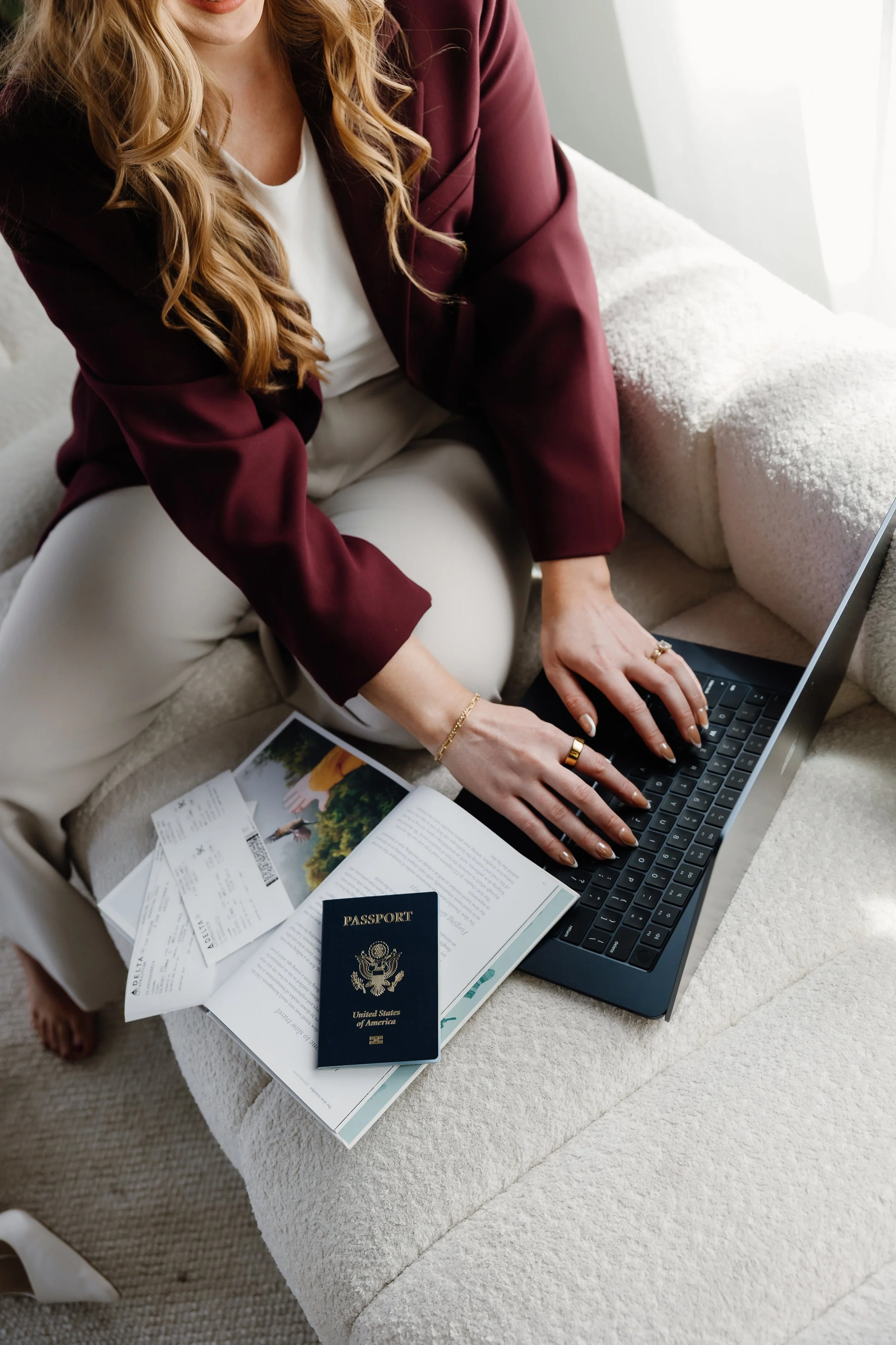 A woman using a laptop at home with travel documents, including a United States passport, boarding passes, and a magazine.