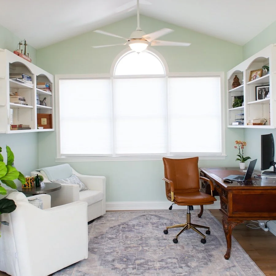 A view of the Kent Island Medical office with large window, white bookshelves, a desk with a computer, and a leather office chair.