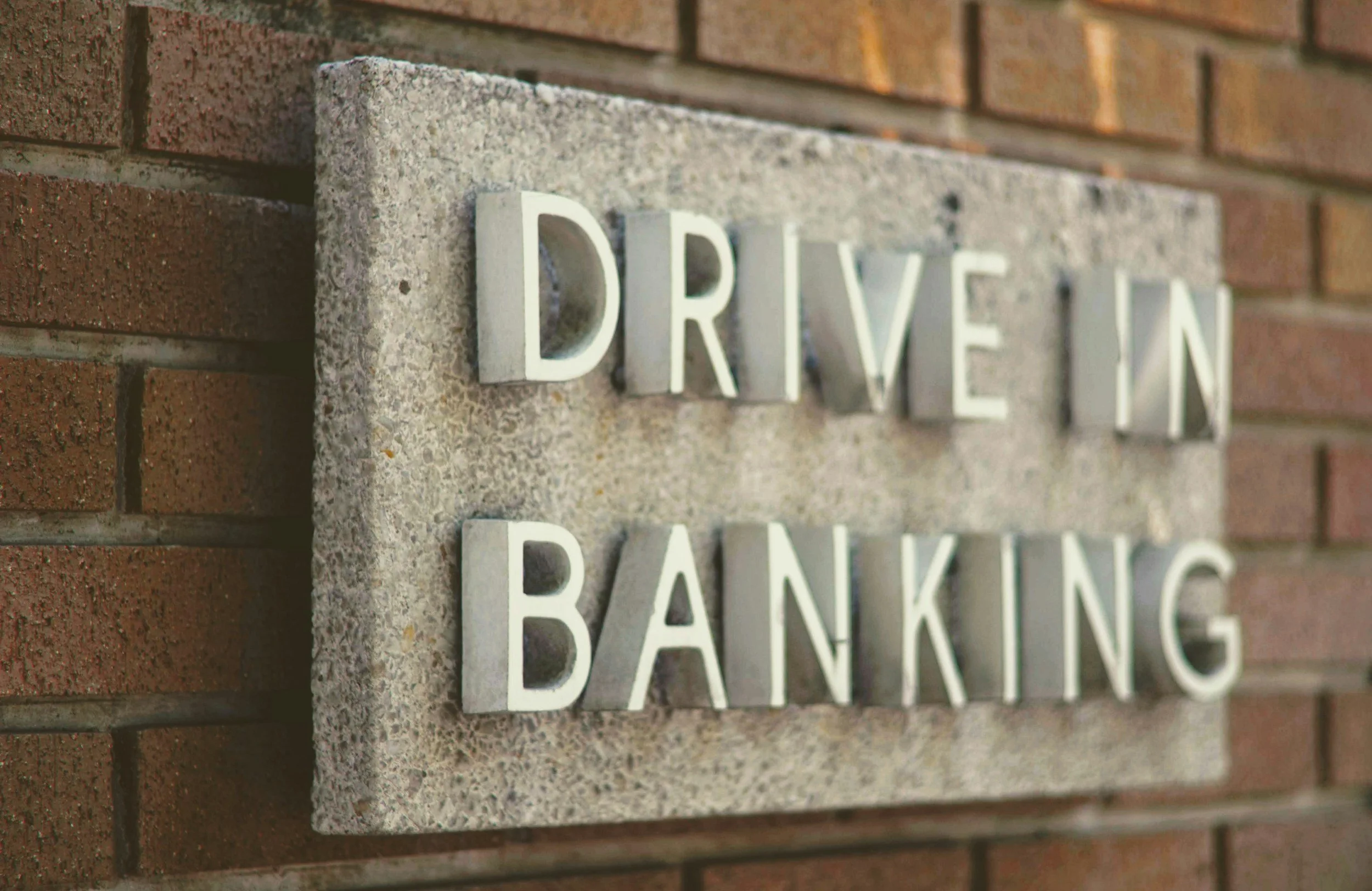 Close-up of a brick wall with a concrete sign reading 'DRIVE TH' and the word 'BANKING' partially visible underneath.