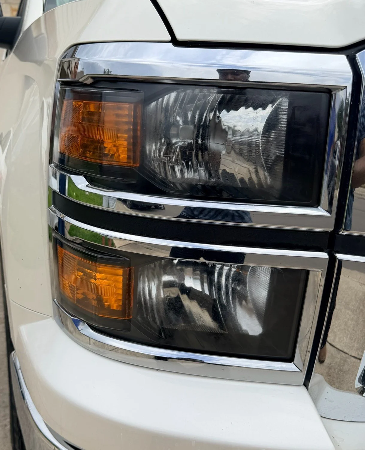 Close-up of a vehicle's front headlight with clear and amber sections, reflecting the surroundings.