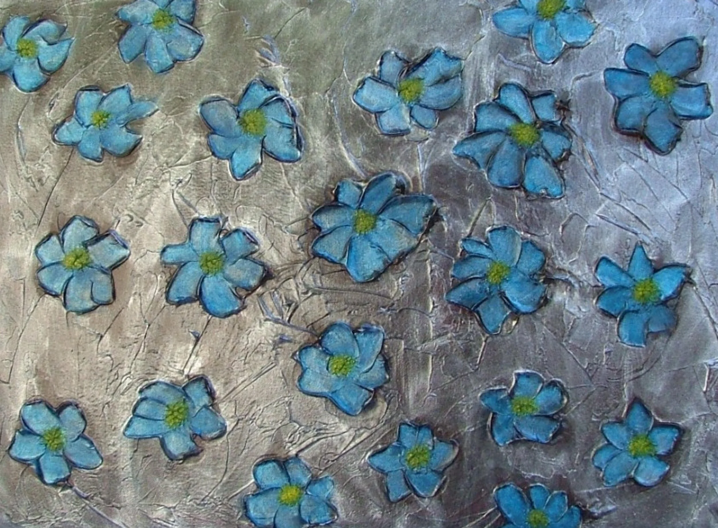 Close-up photo of a textured surface decorated with small blue flowers with green centers, arranged scattered across a metallic background.