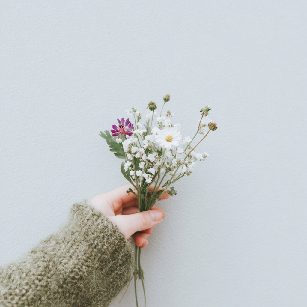 Person holding a small bouquet of mixed wildflowers against a plain white background.