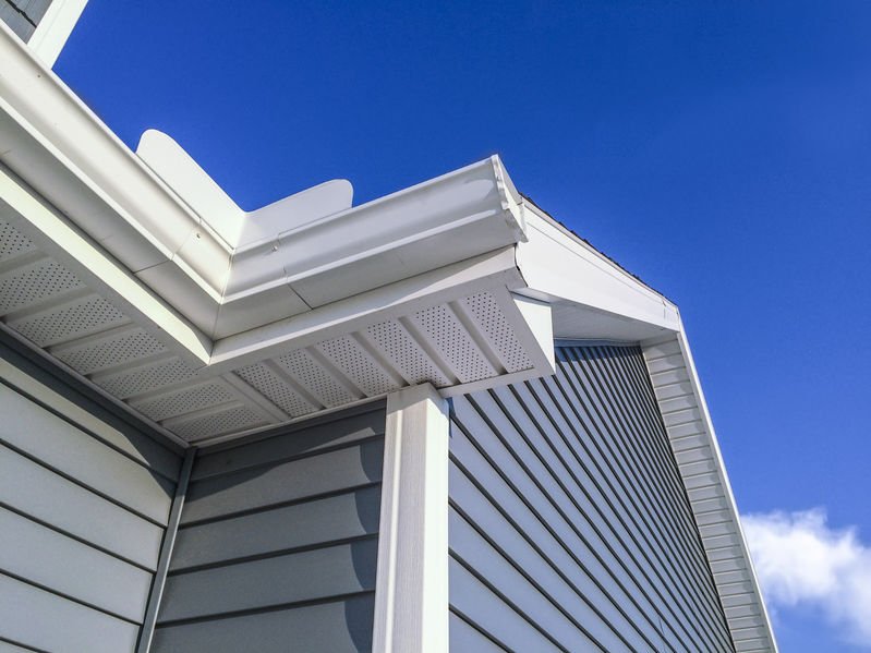 Close-up of the corner of a house with gray siding, white trim, and a blue sky in the background.